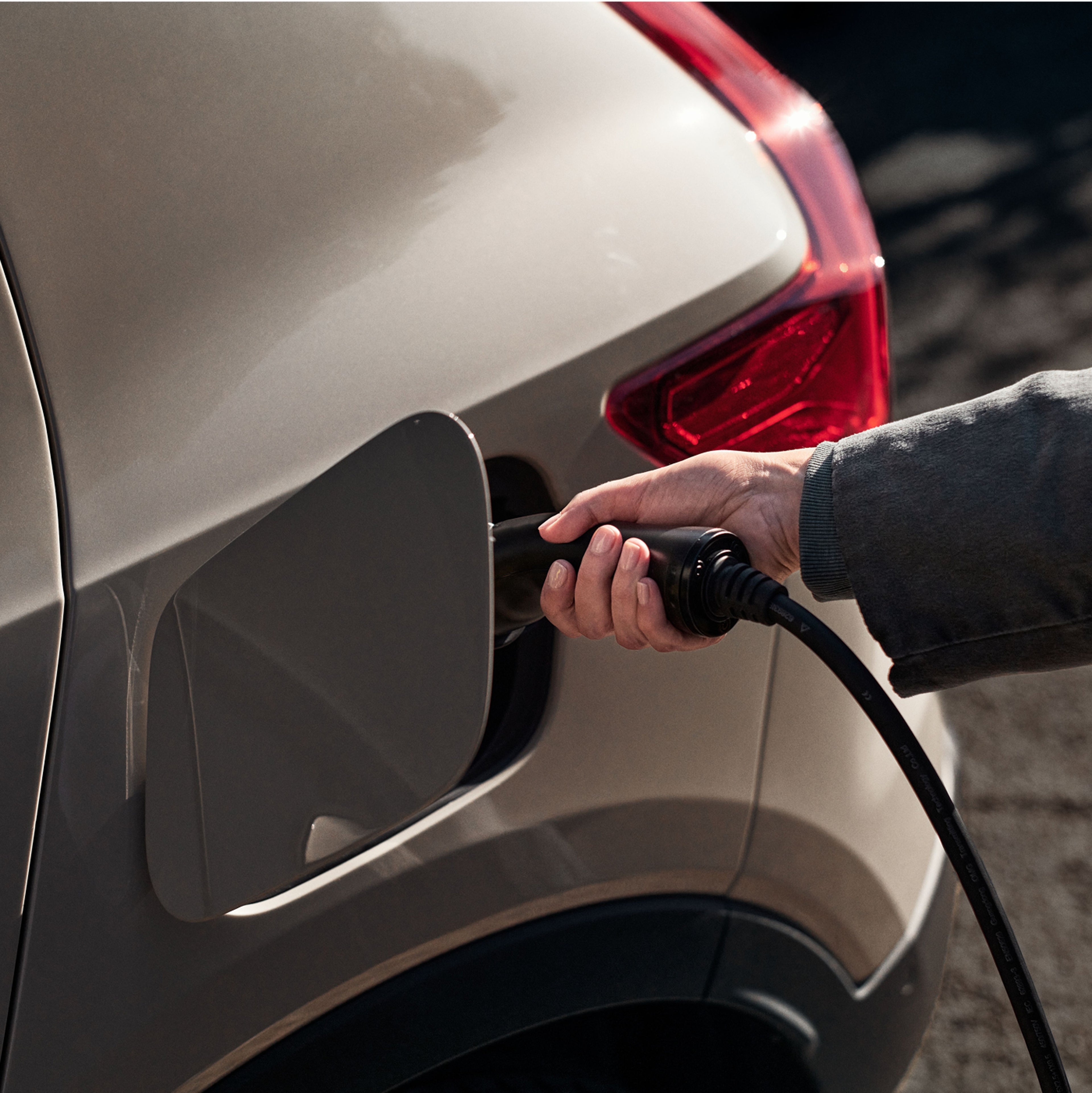 Close up of a hand plugging a charging cable into an electric vehicle.