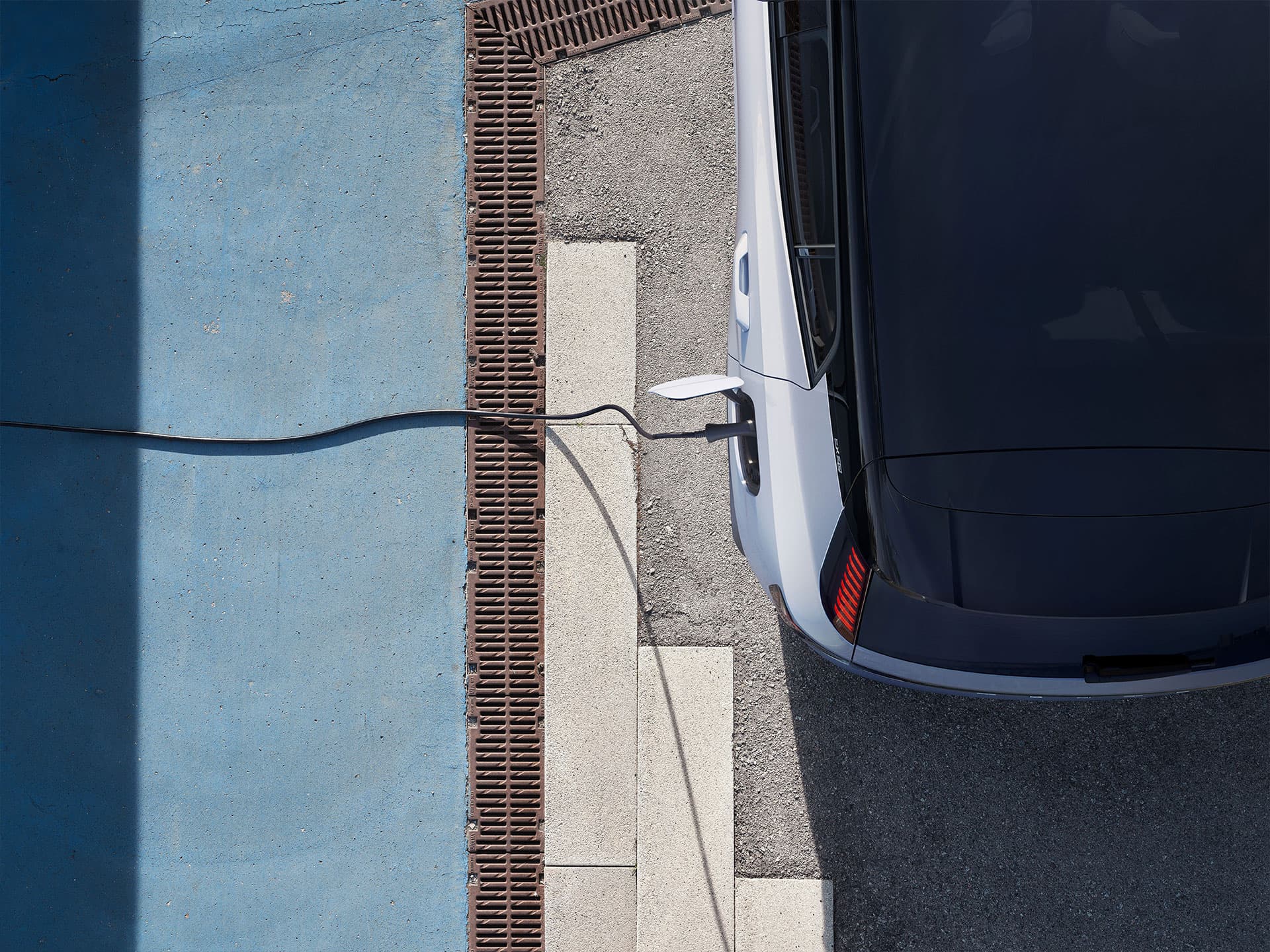Weitwinkelansicht eines vollelektrischen Volvo EX30, der an einer Ladestation angeschlossen ist, von hinten links.