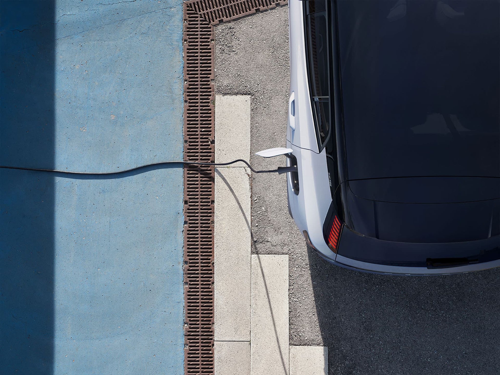 Uma perspetiva panorâmica da parte traseira esquerda de um Volvo EX30 100% elétrico ligado à tomada para carregamento.