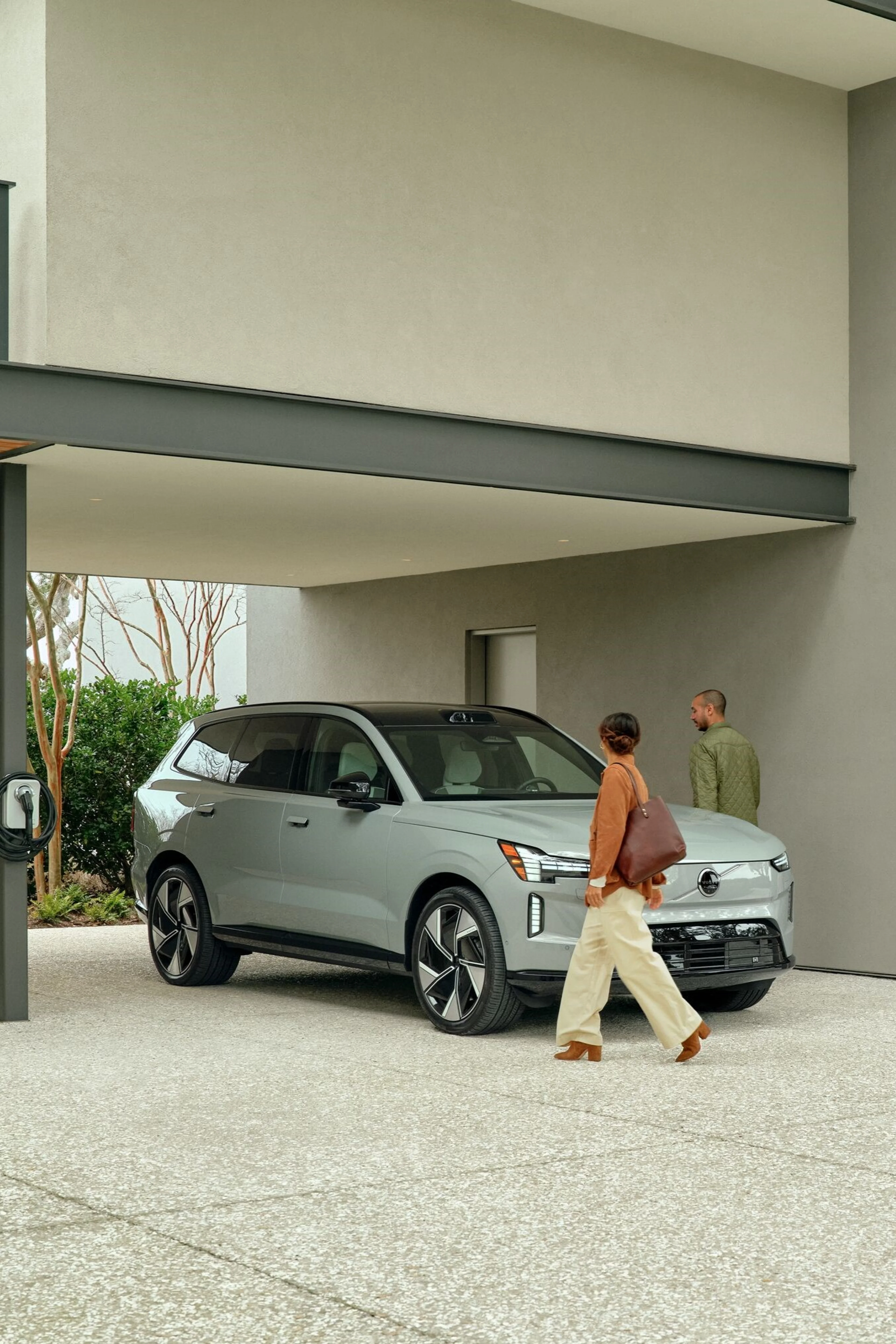 Family approaching fully electric Volvo EX90 SUV parked near house with charger