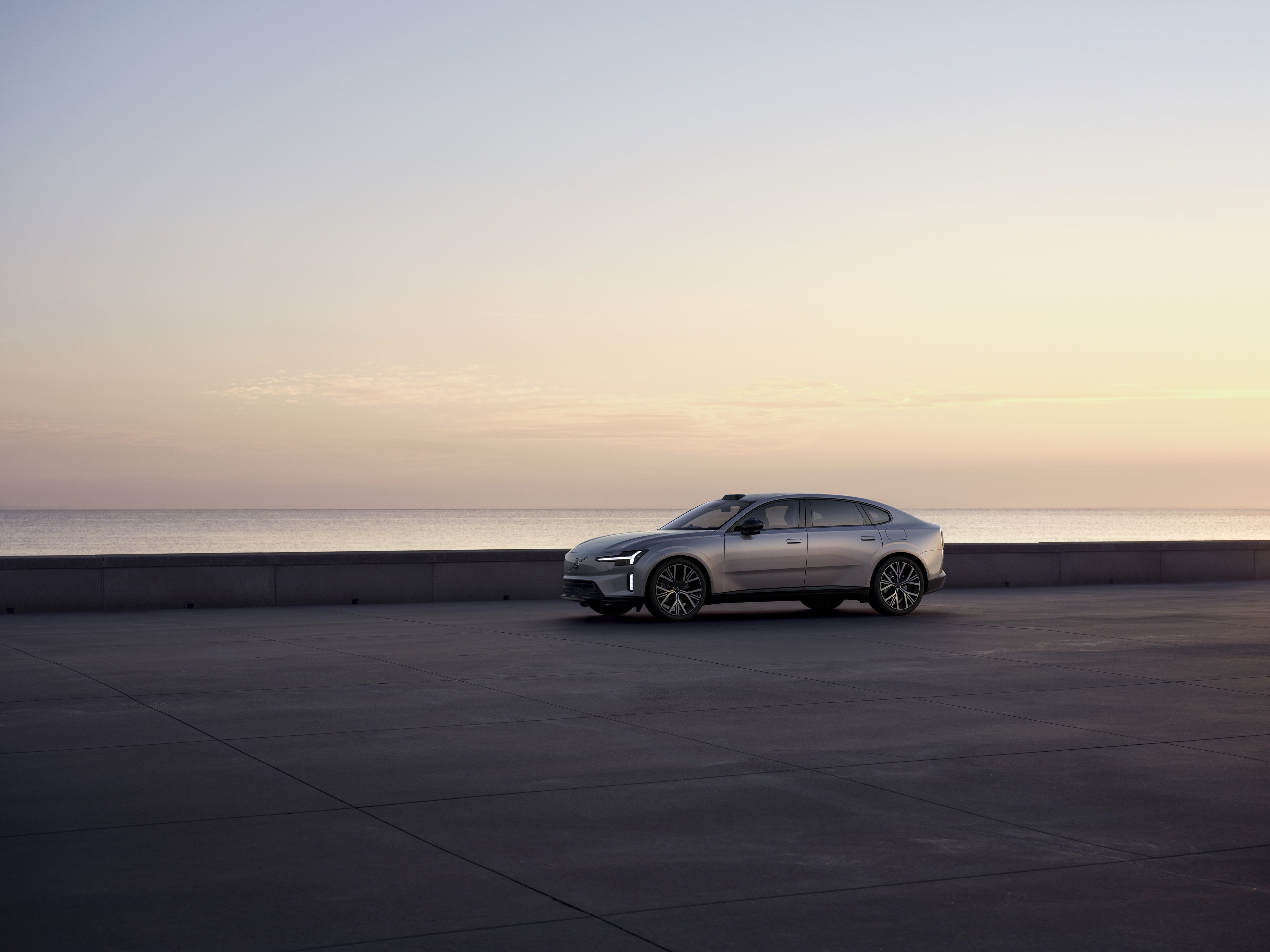 Plan large d'une berline Volvo S90 Bleu Denim roulant sur une route forestière par une journée ensoleillée.
