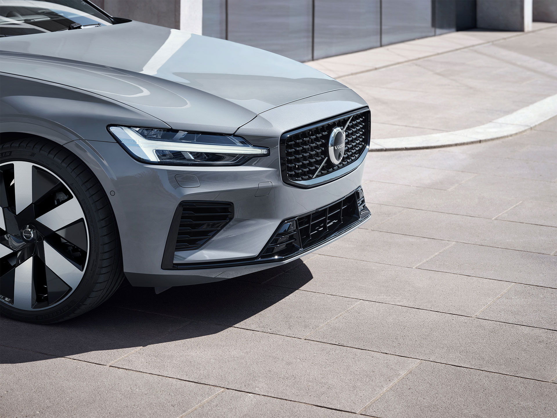 The front, side exterior of a Volvo plug-in hybrid displaying Thor’s Hammer LED headlamps in an outdoor urban setting.