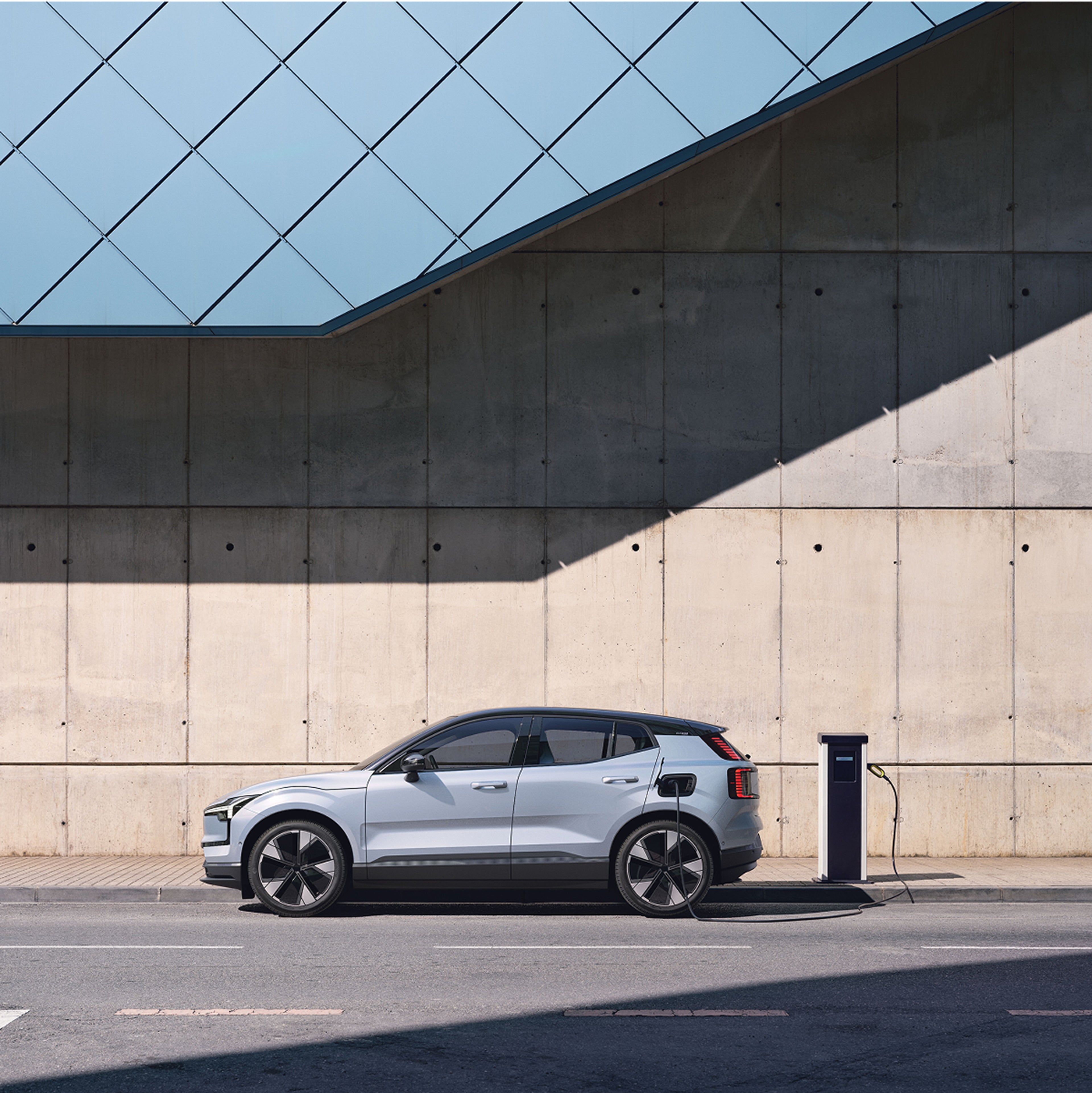 Left side view of an electric SUV plugged into a public charging
point on the side of a road next to a concrete building.