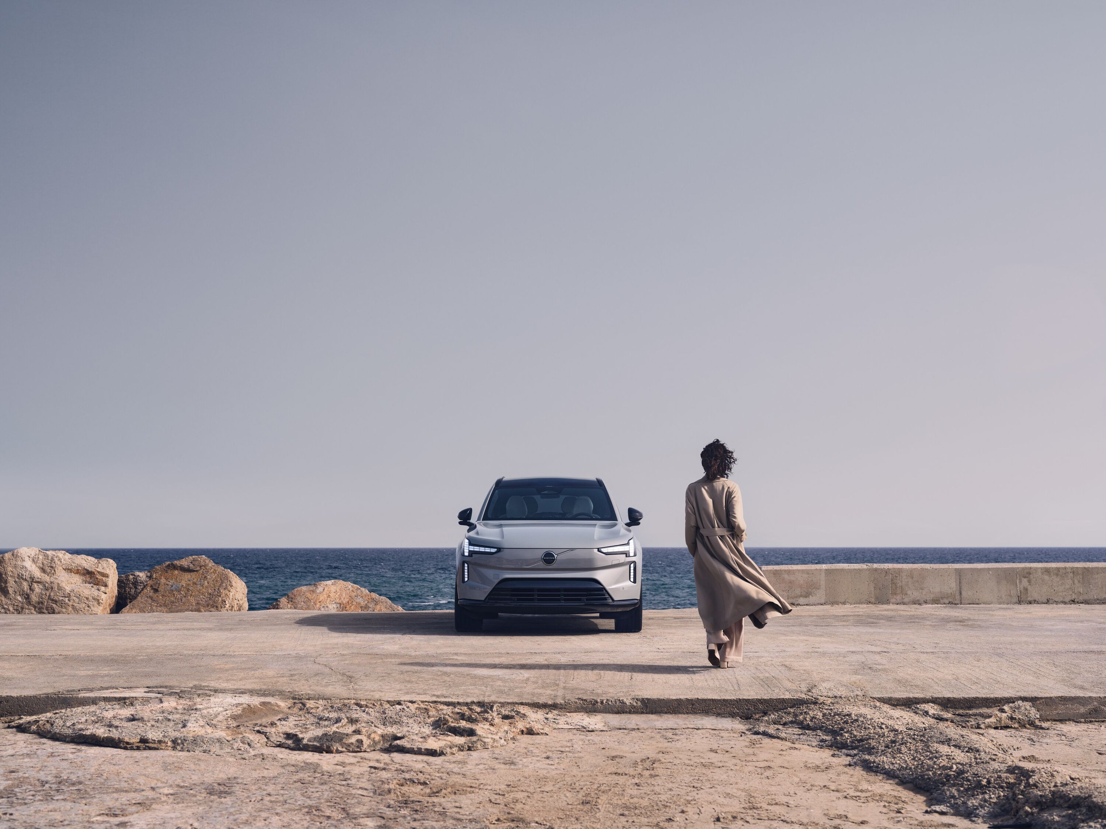 Une femme floue se tient au milieu d’une rue avec un Volvo EX90 visible derrière elle.