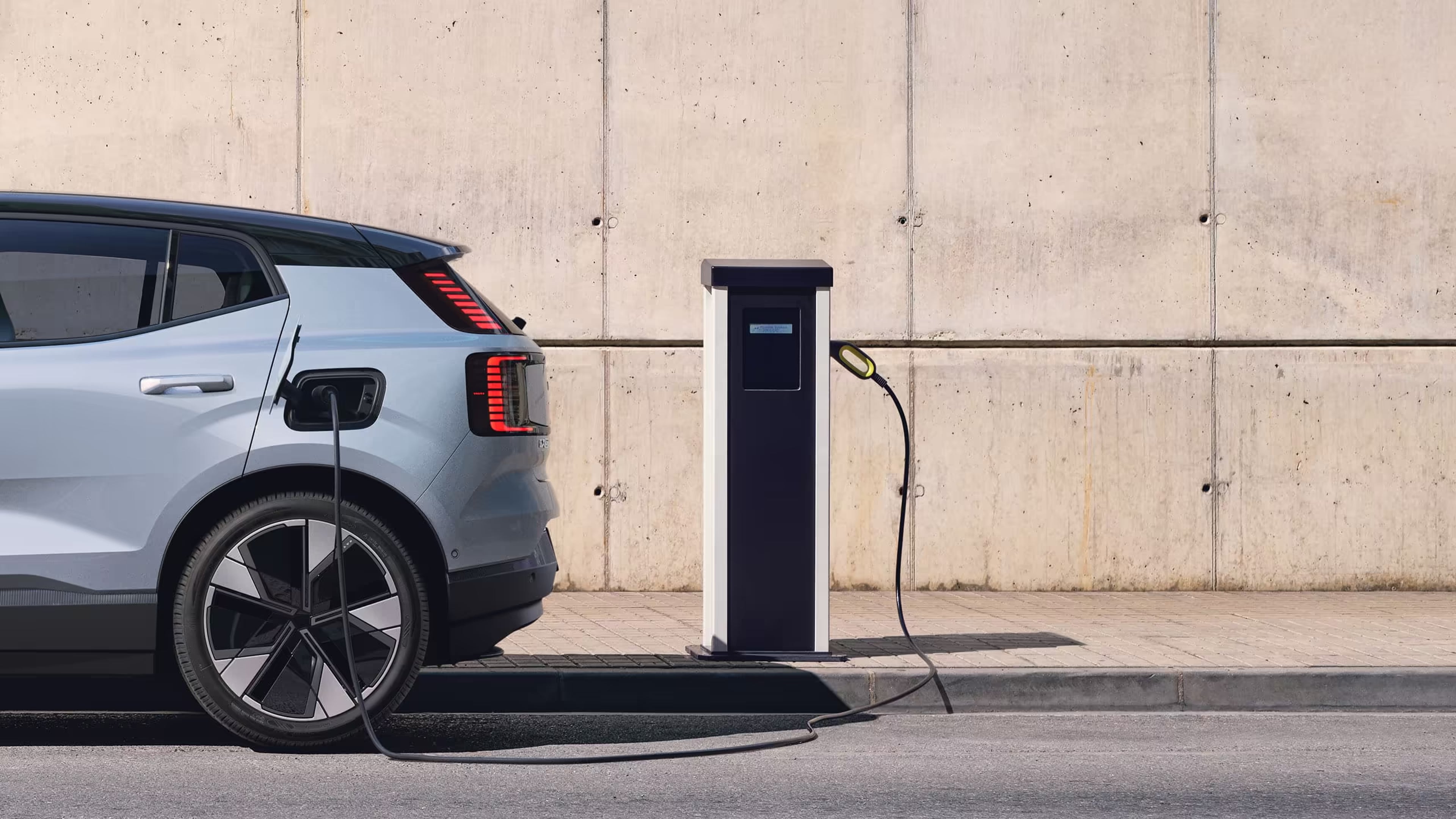 Lähikuva Cloud Blue -värisestä Volvo EX30-mallista kytkettynä latausasemaan.