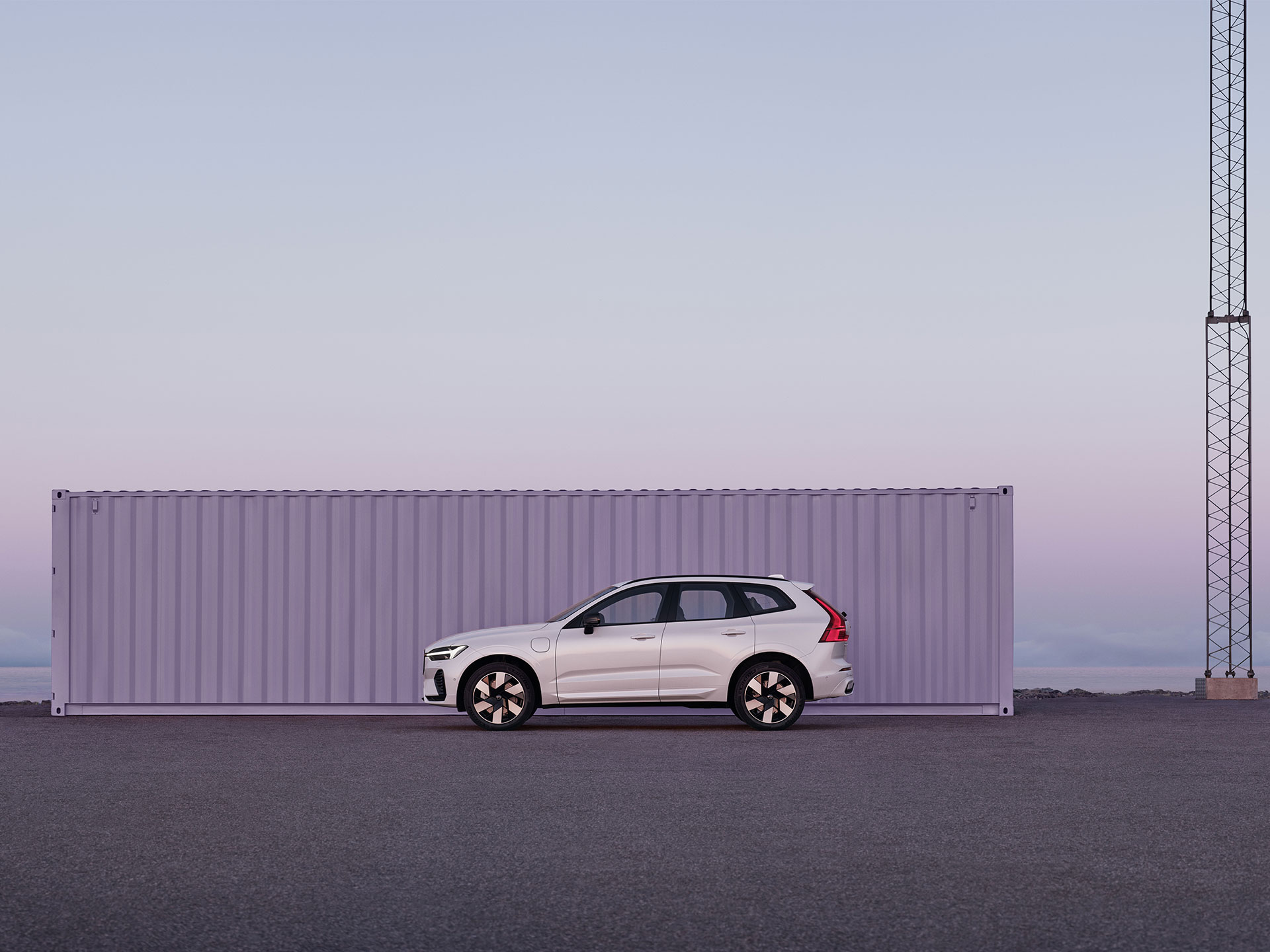 Volvo XC60 pysäköitynä syrjäiseen teollisuusympäristöön, taustalla auringonnousun violettia ja vaaleanpunaista valoa.