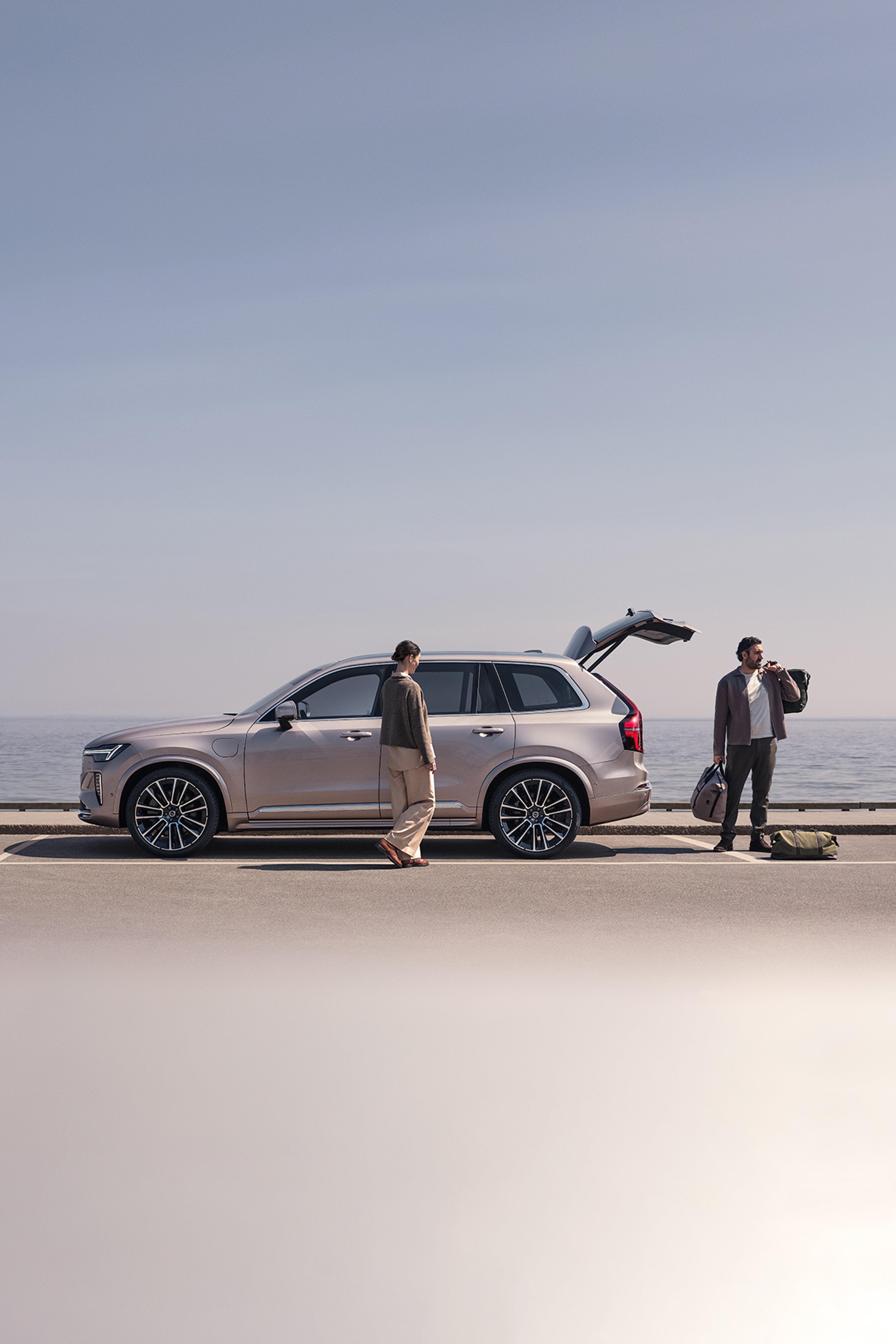 A family at the beach near a Volvo XC90 Plug-in hybrid, changing from skiing clothes to swimming clothes.