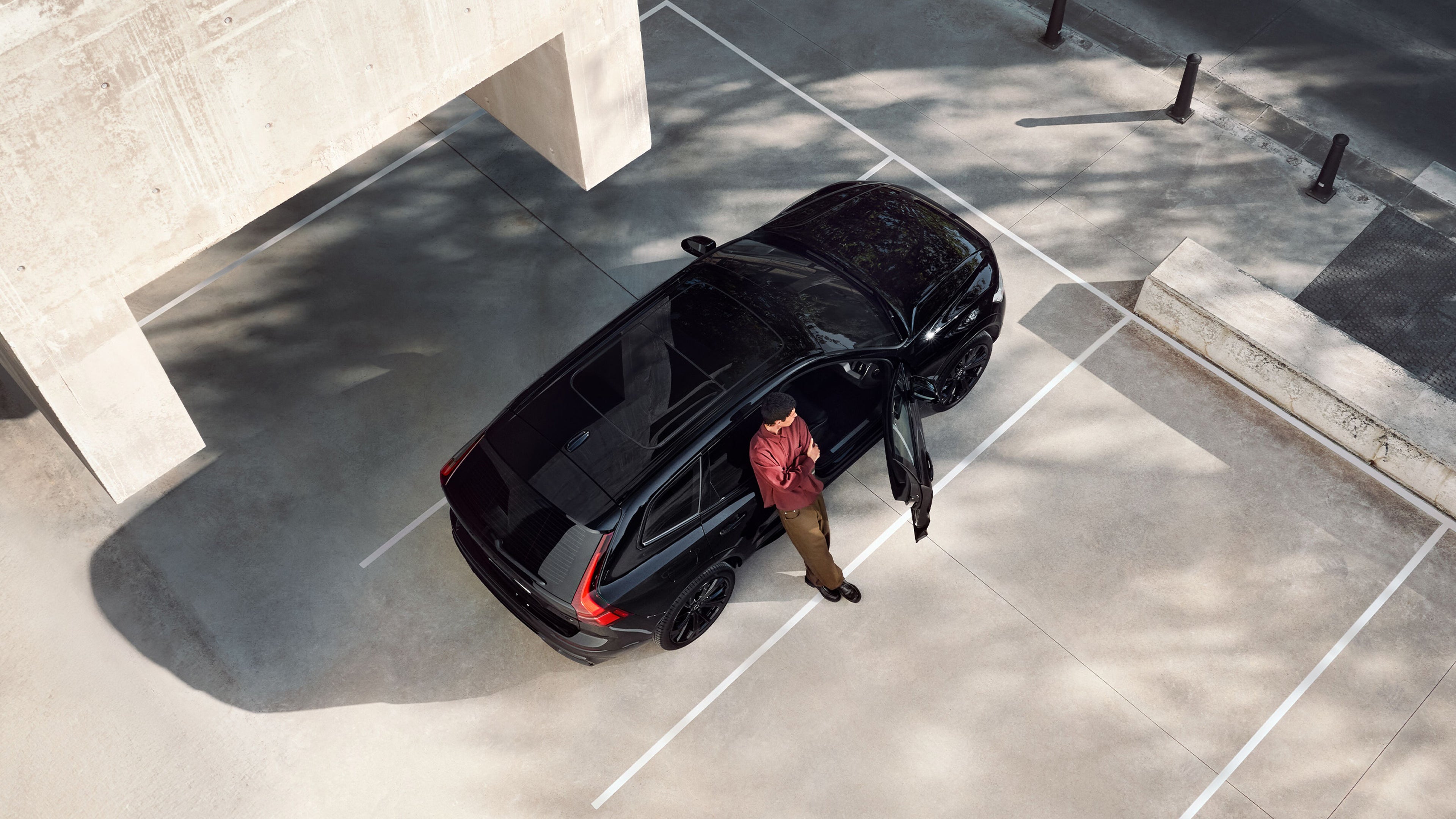 Маж стои покрај отворените врати од Volvo XC60 Black Edition на паркинг.