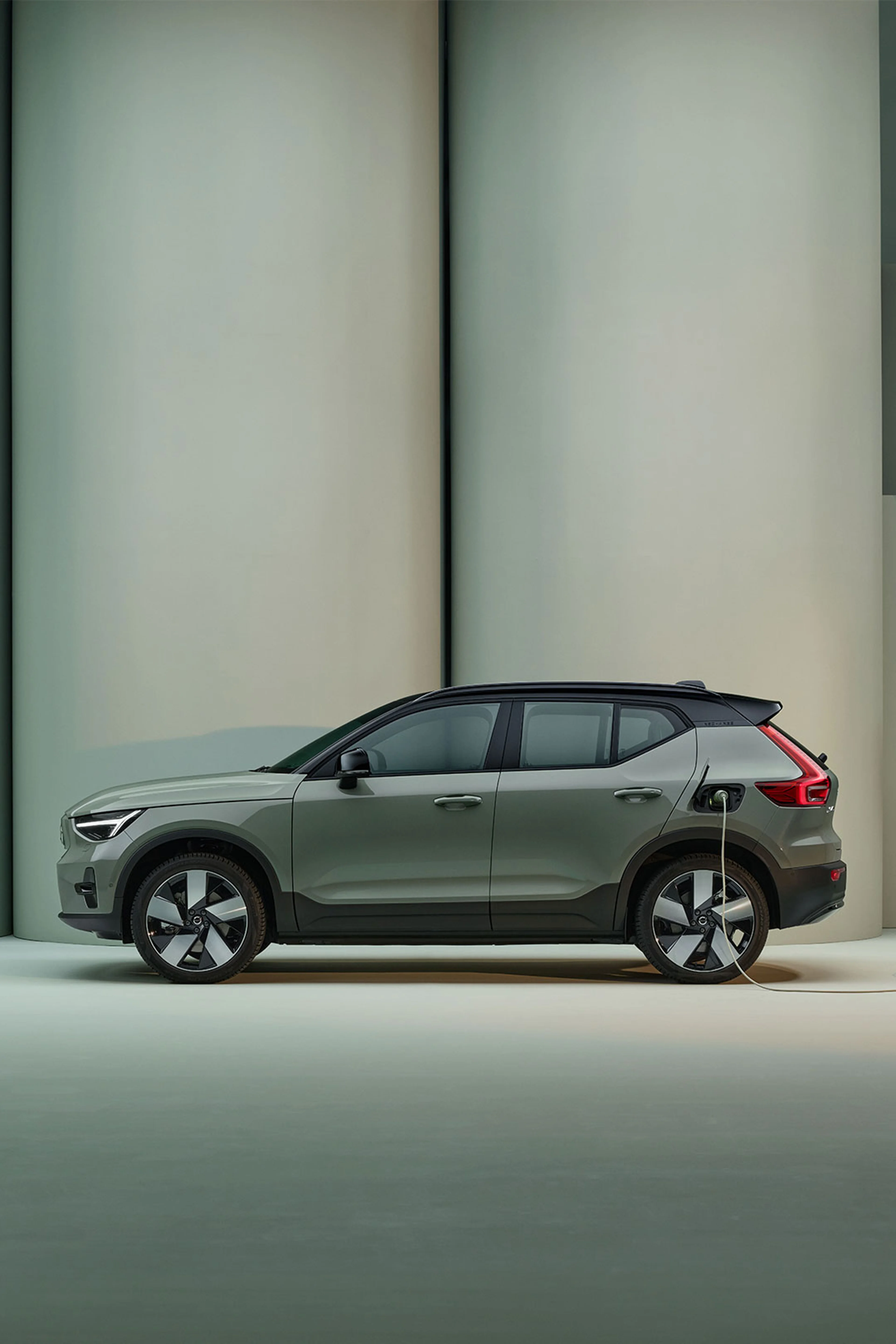 The side of a sage green Volvo XC40 connected to a charging cable.