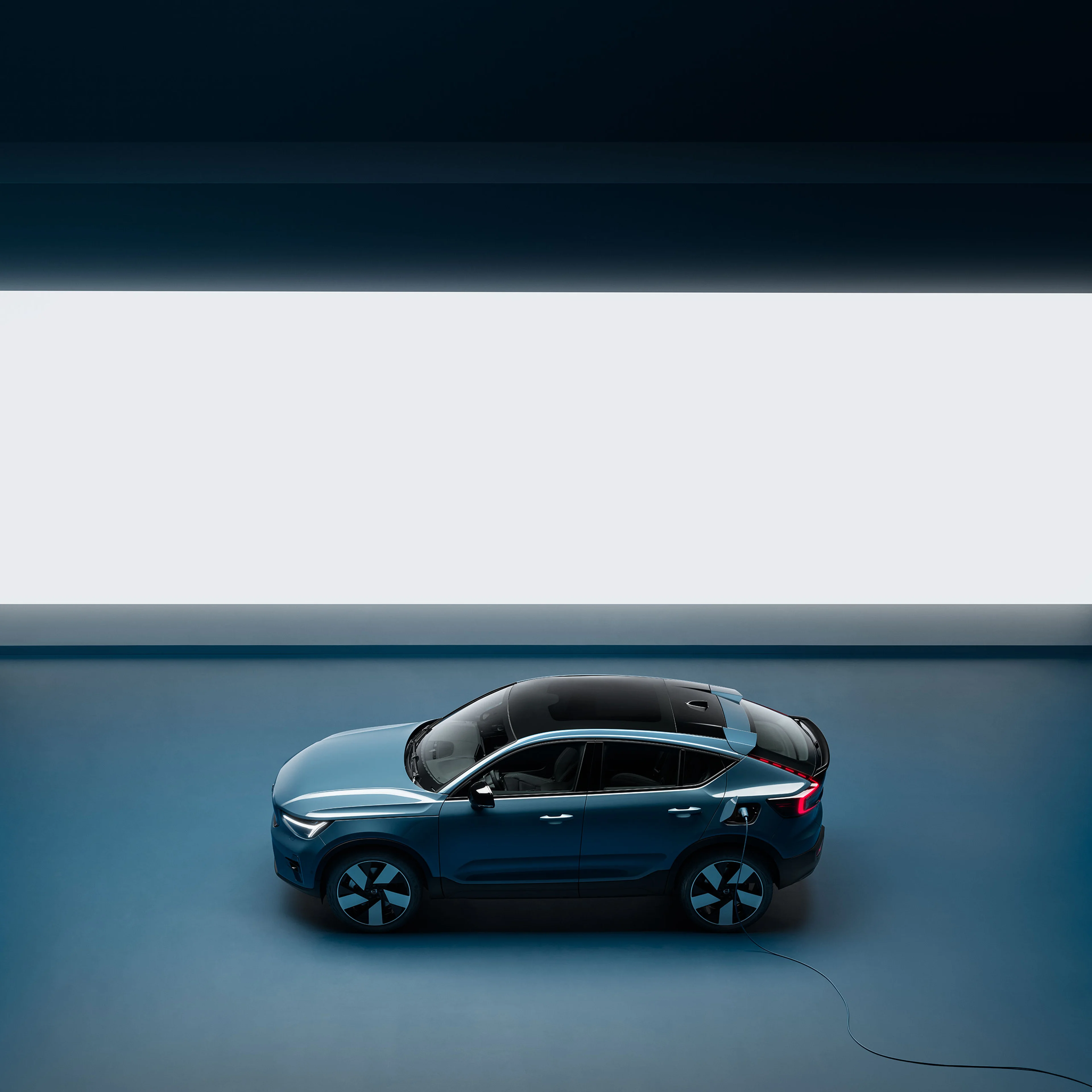 An electric Volvo car being charged with a charging cable in an interior setting.
