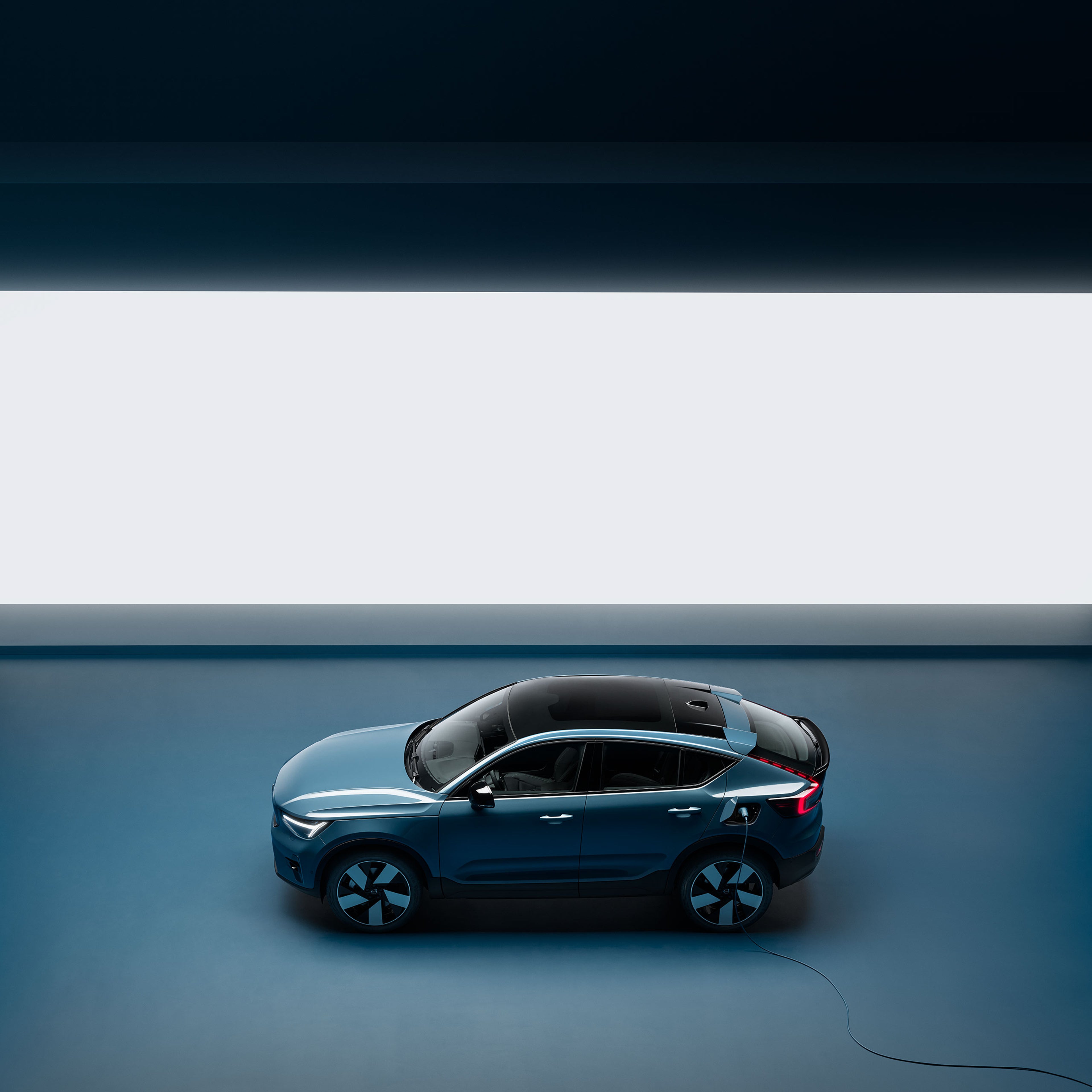 Um automóvel elétrico Volvo a ser carregado com um cabo de carregamento num ambiente interior.