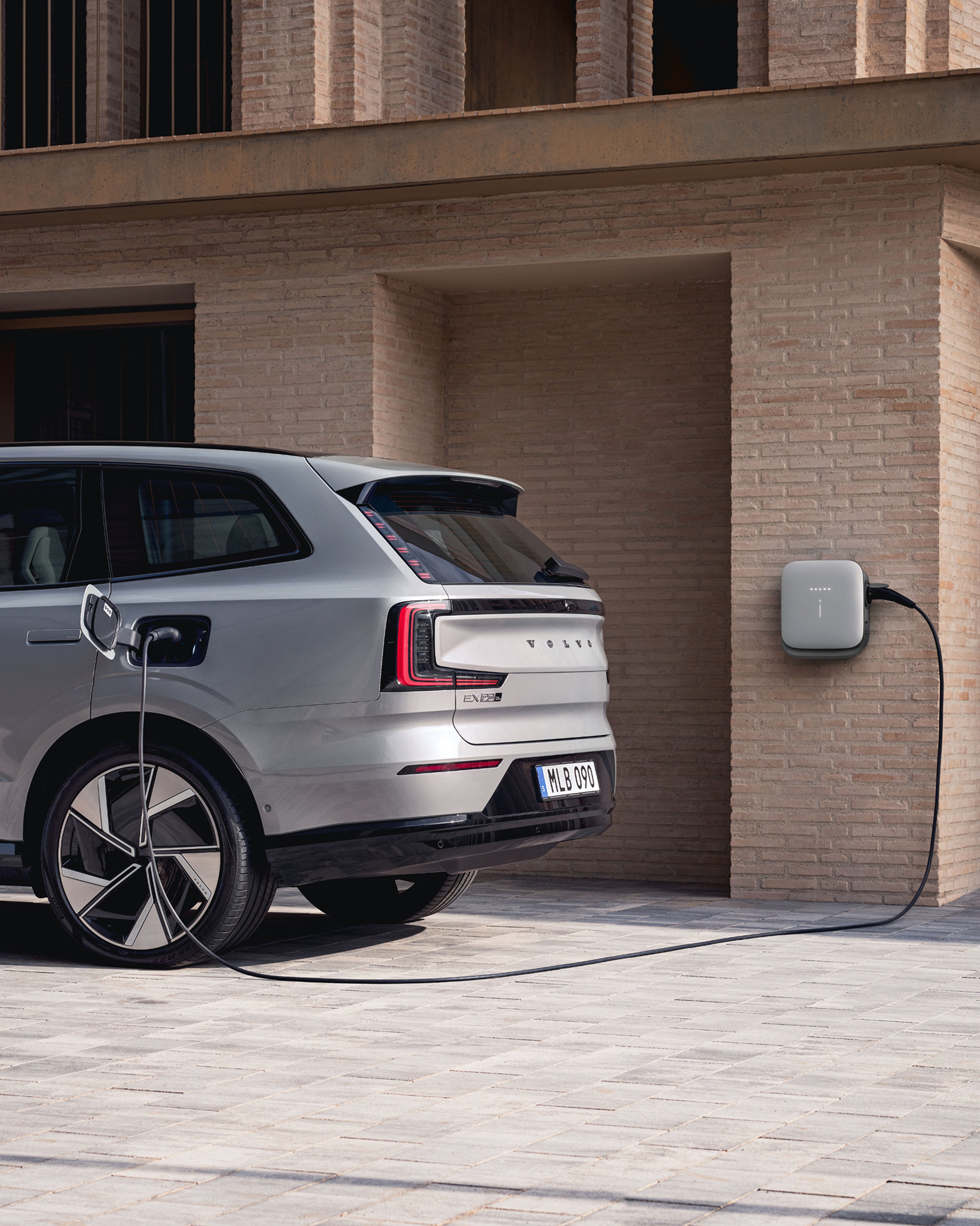 Eestvaade valges minimalistlikus garaažiruumis koduse seinakasti kõrvale pargitud valgele elektrilisele Volvo linnamaasturile.