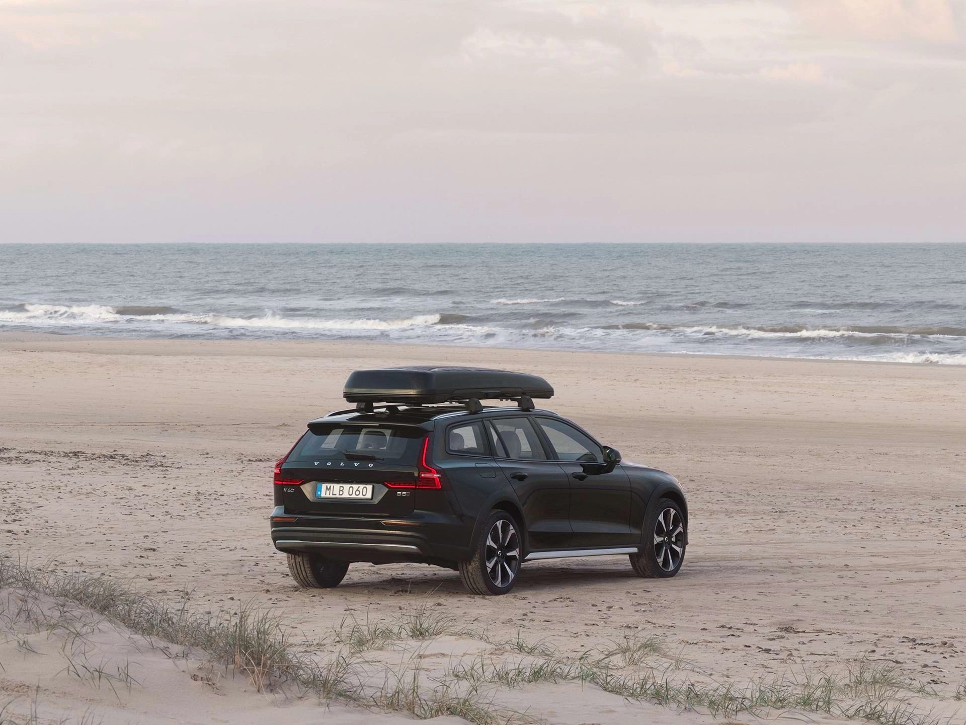 Un vehículo familiar Volvo con un baúl de techo estacionado sobre la arena en una playa.