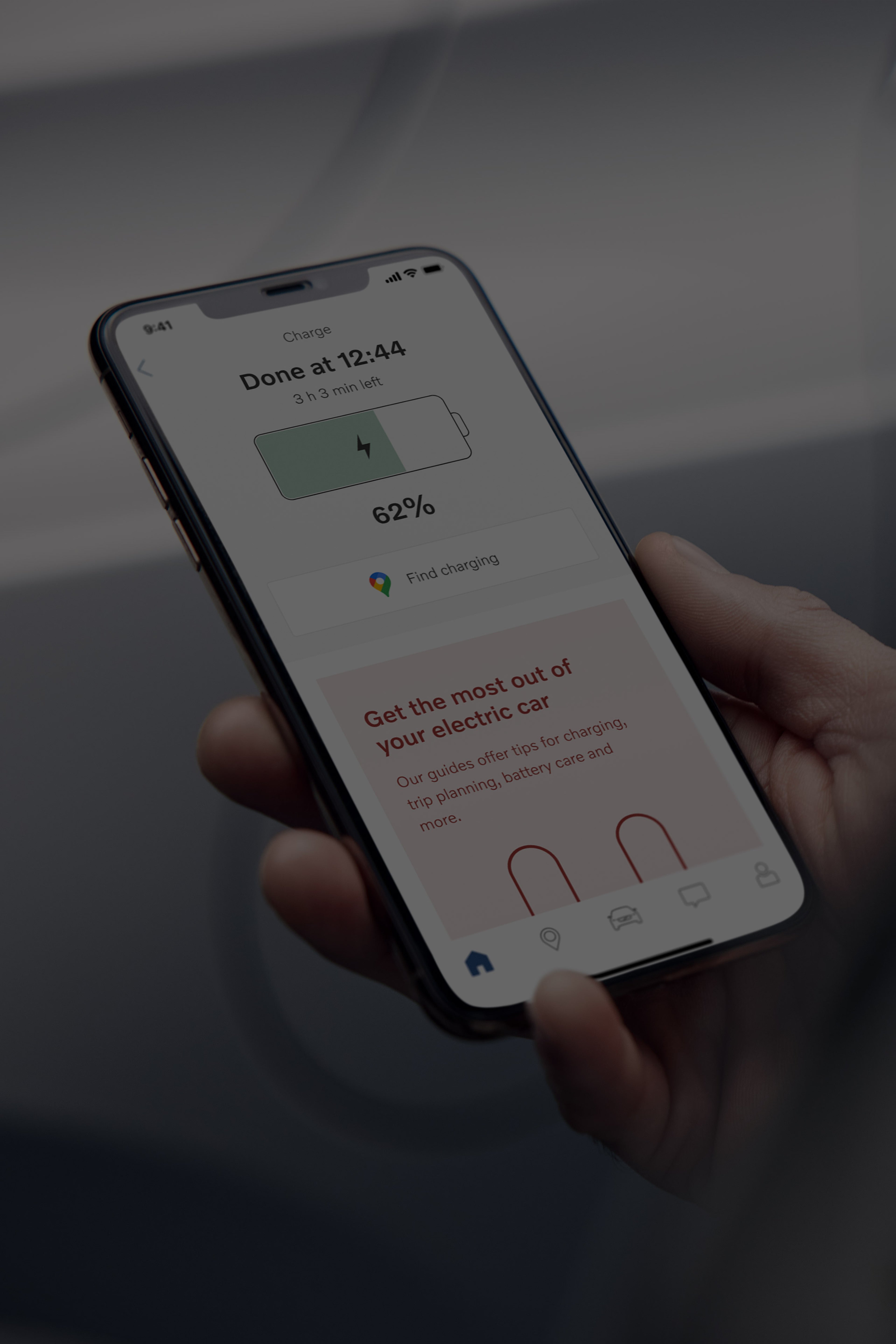 Vaizdas per „Volvo“ automobilio savininko petį, kai jis stebi savo automobilio baterijos įkrovimo būseną „Volvo Cars“ programėlėje.