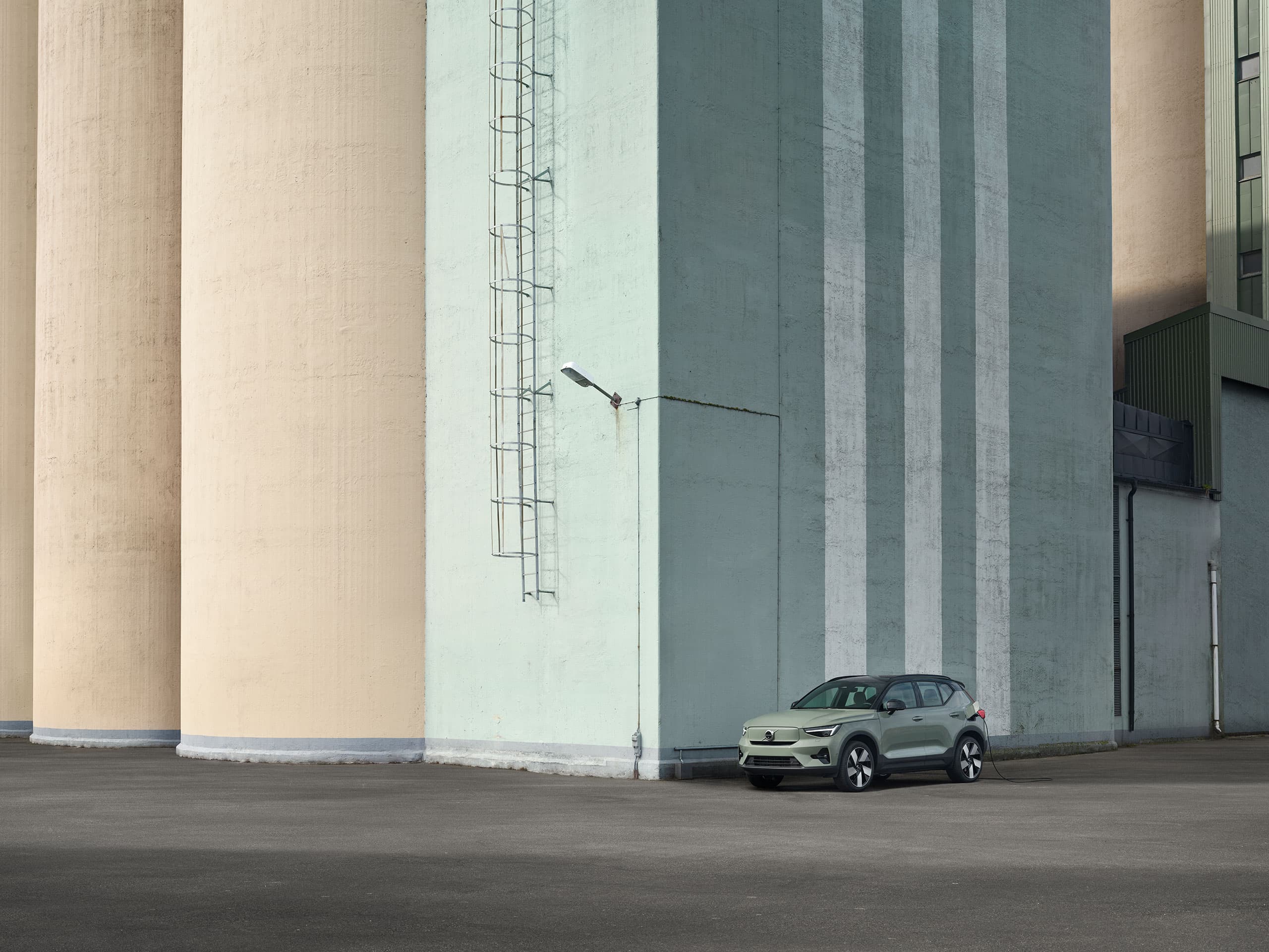 Volvo EX40 Vert Sauge garé à côté d'un grand bâtiment en béton.