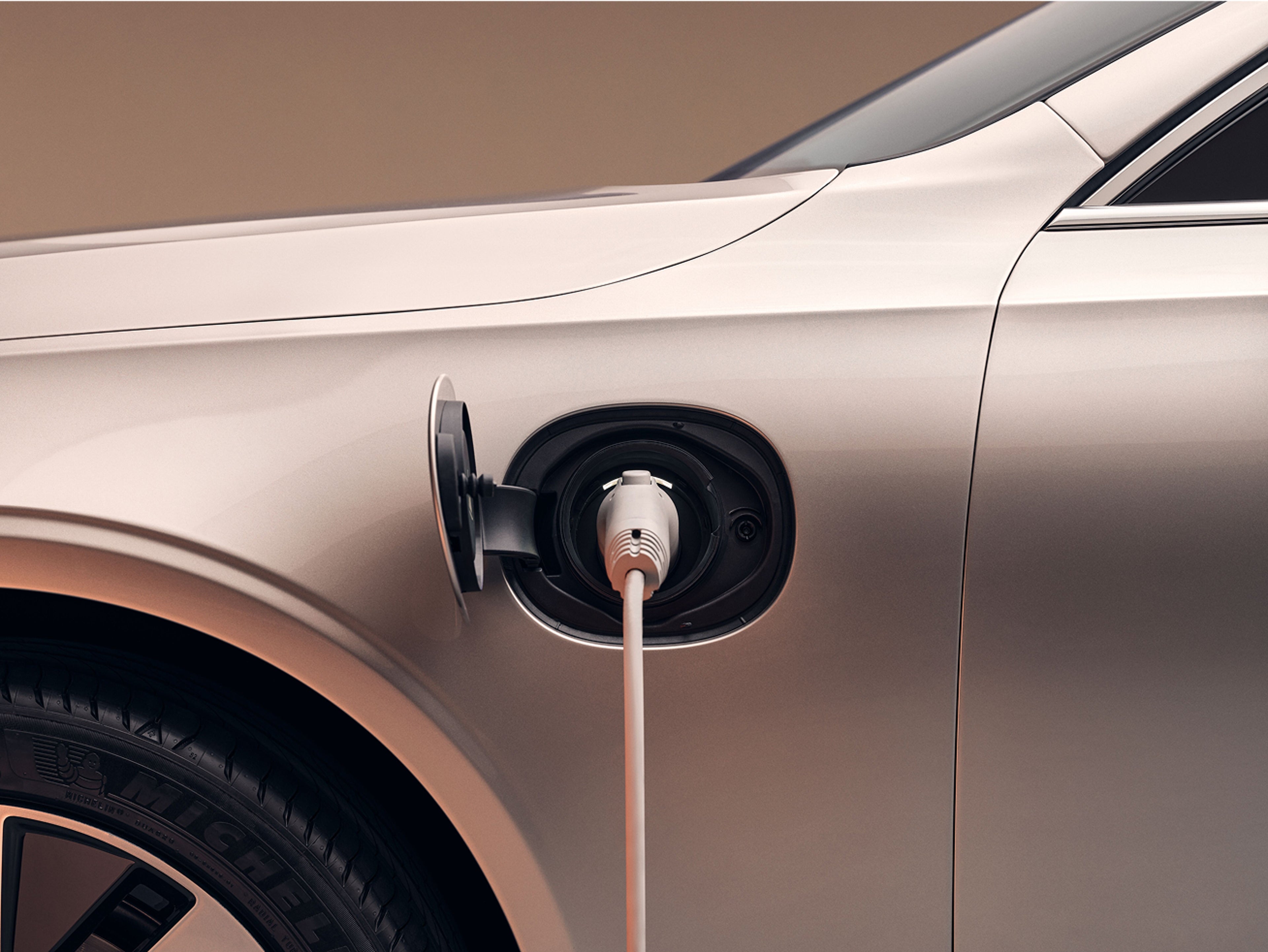 Close-up of a charging cable plugged into the port of a Volvo electric vehicle, showing the side of the car during charging.