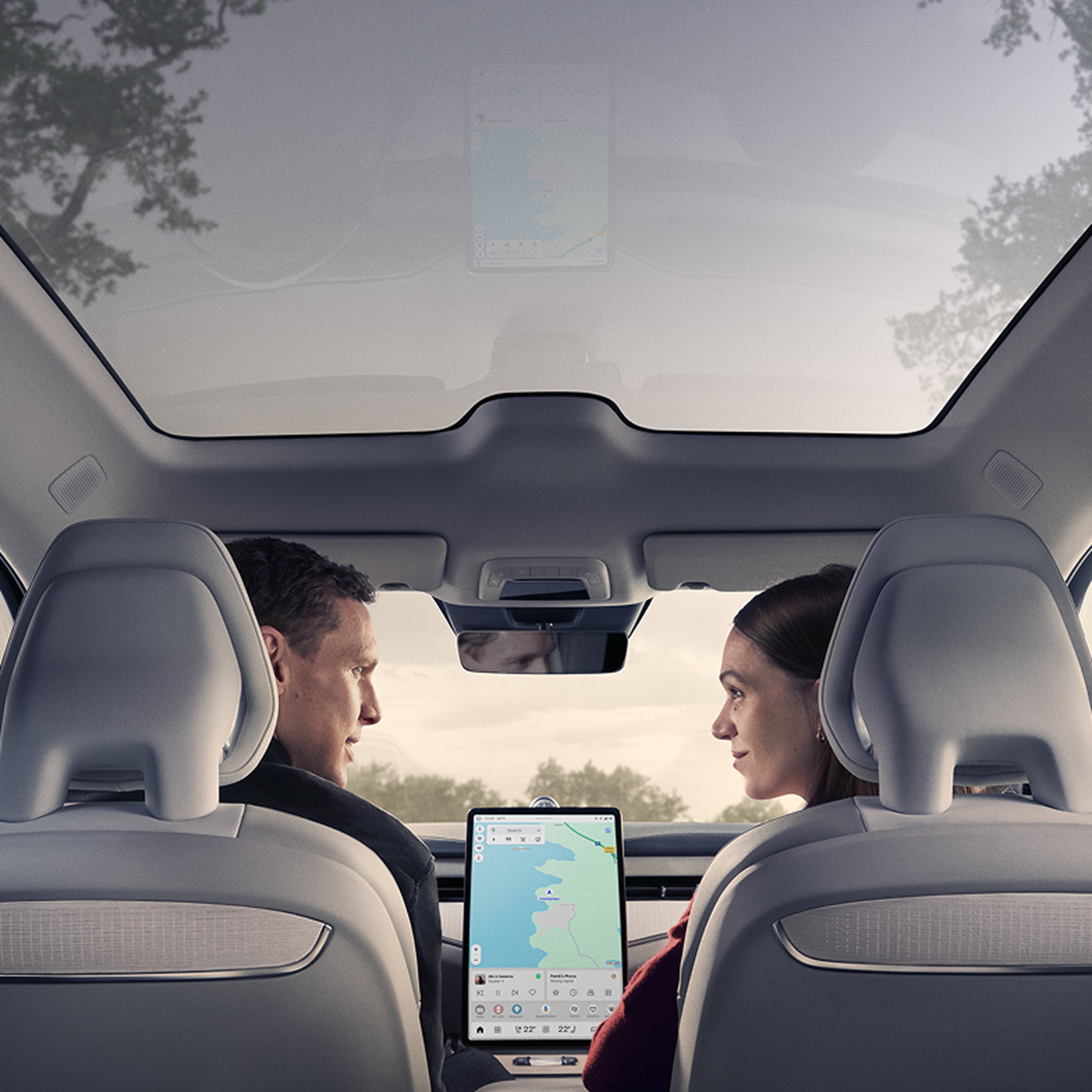 Vue intérieure d’une Volvo montrant un homme et une femme assis sur les sièges avant, face à face, avec un grand système de navigation à écran tactile entre eux.