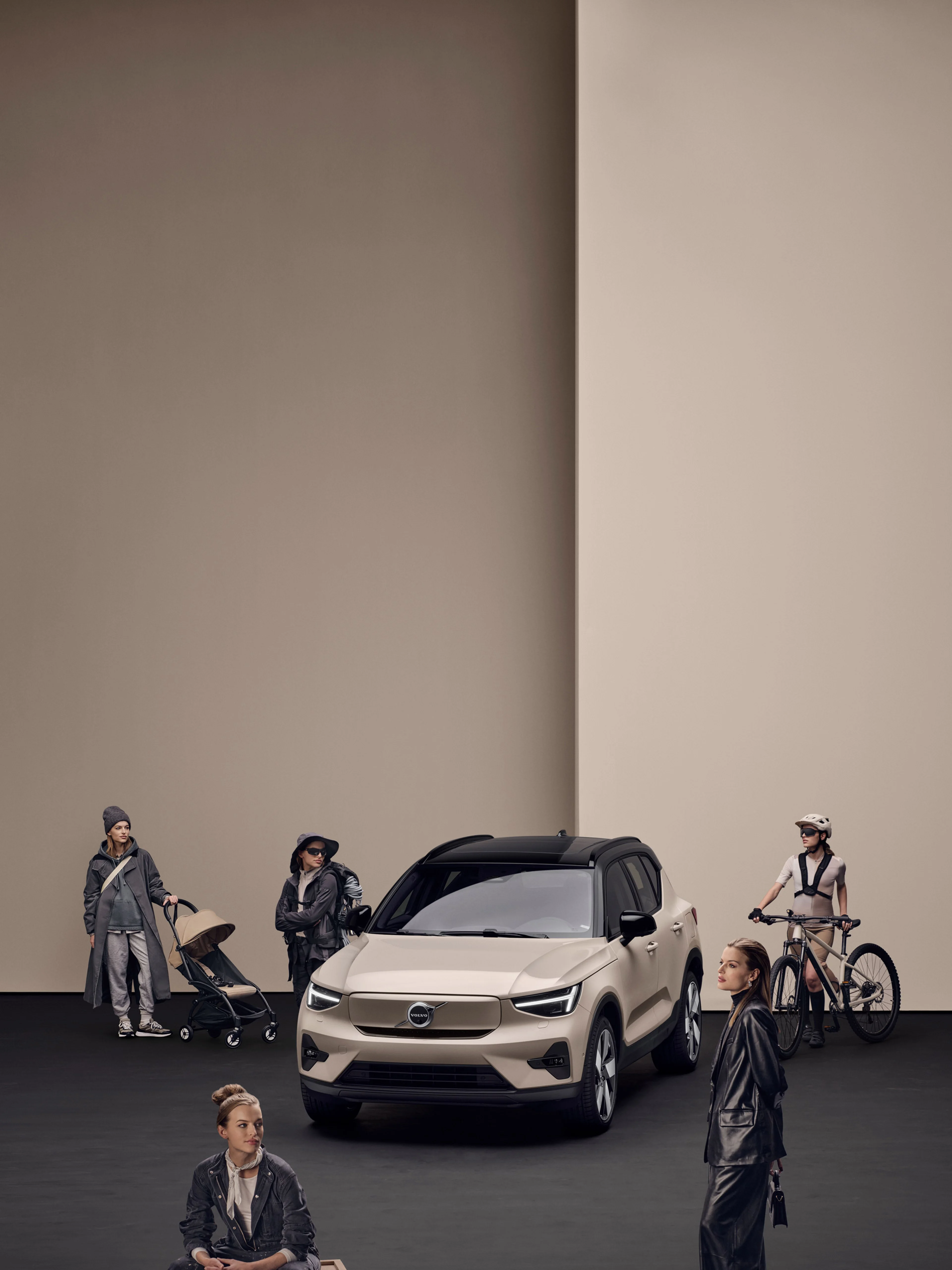 Beige Volvo EX40 elbil i en studio med svart golv och beige bakgrund, omgiven av personer i olika livsstilssituationer, inklusive en cyklist, en person med barnvagn och andra i vardagskläder.