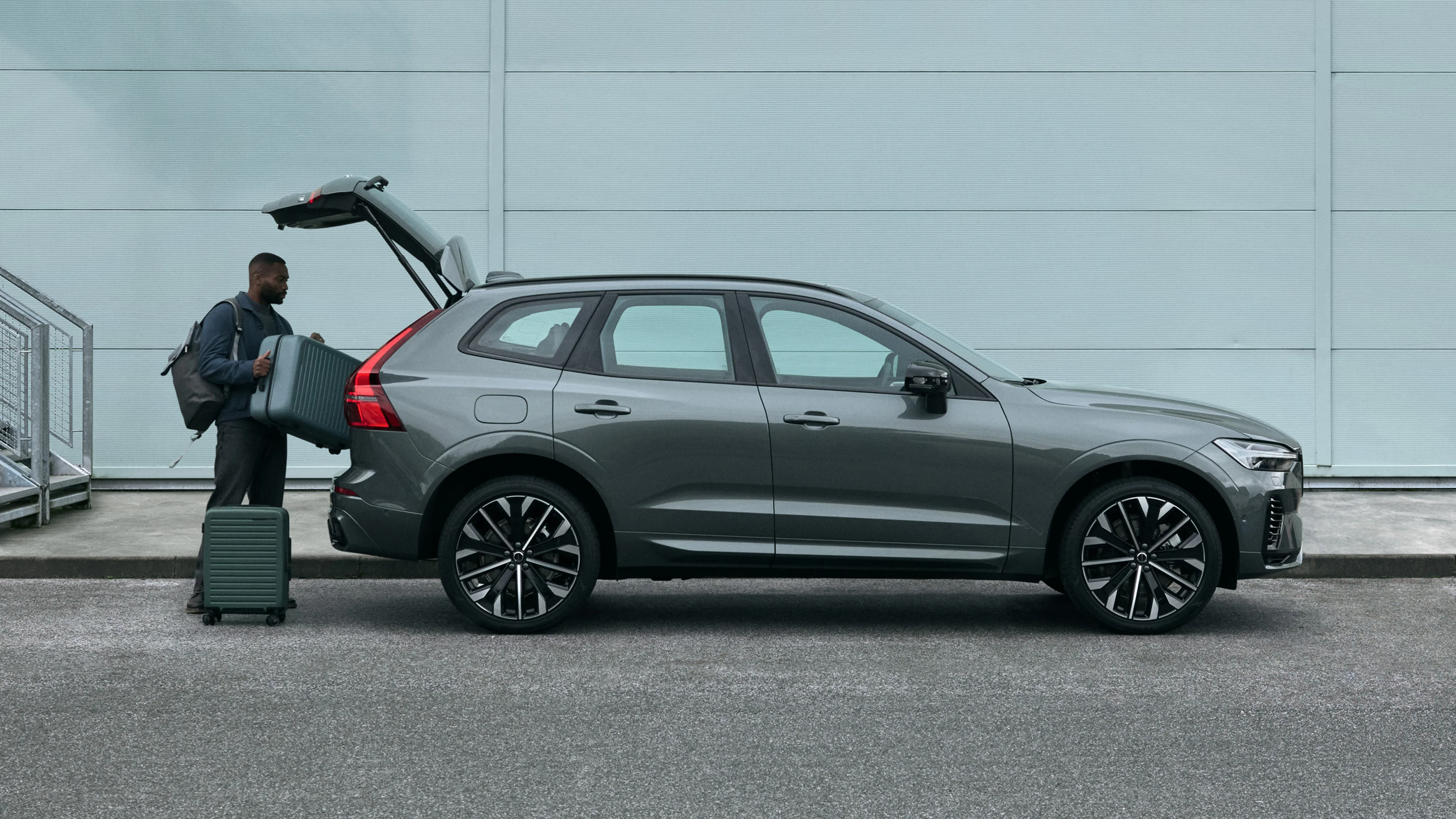 En man lastar in väskor i en Volvo XC60 framför en industribyggnad