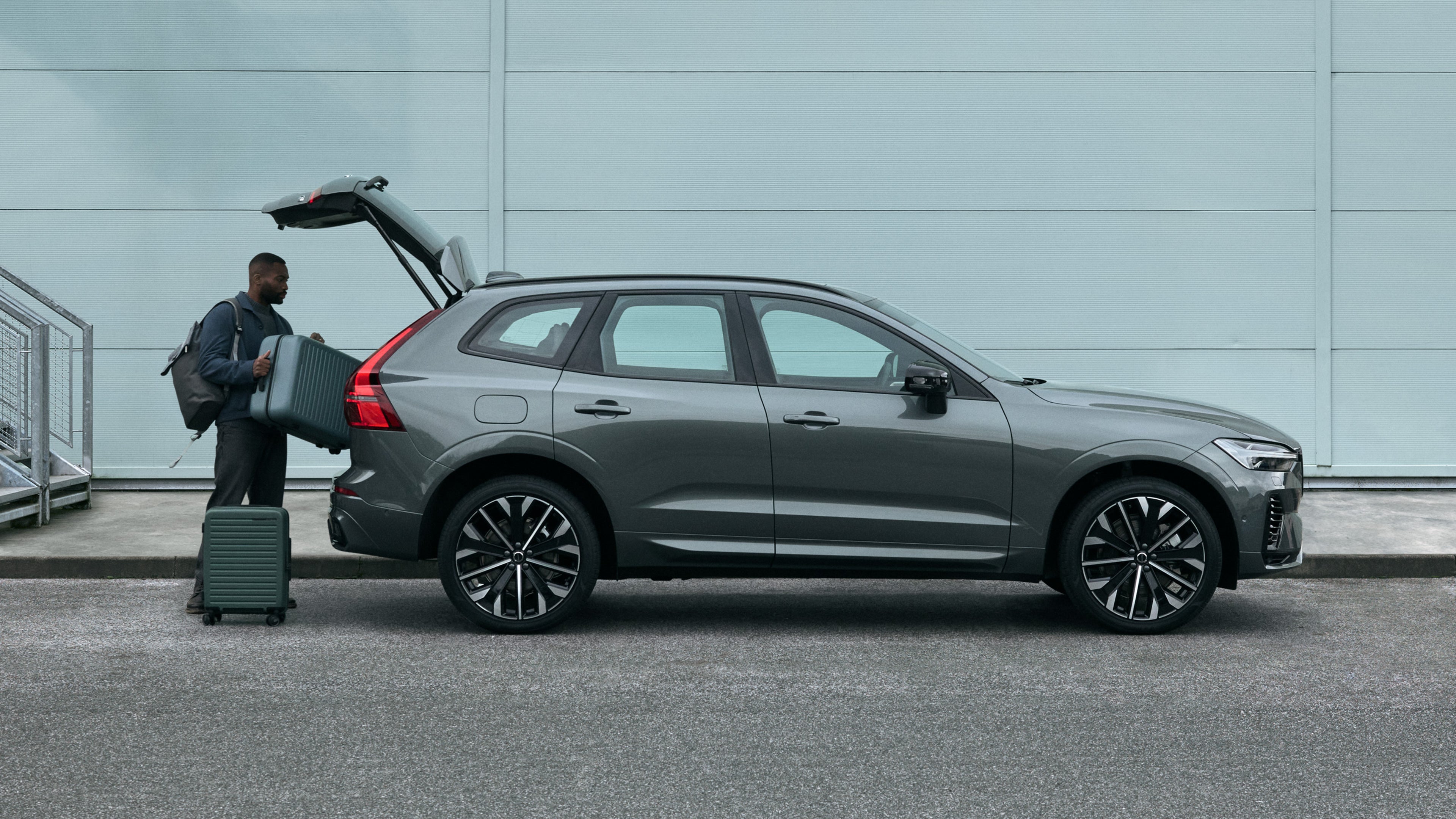 En man lastar in väskor i en Volvo XC60 framför en industribyggnad