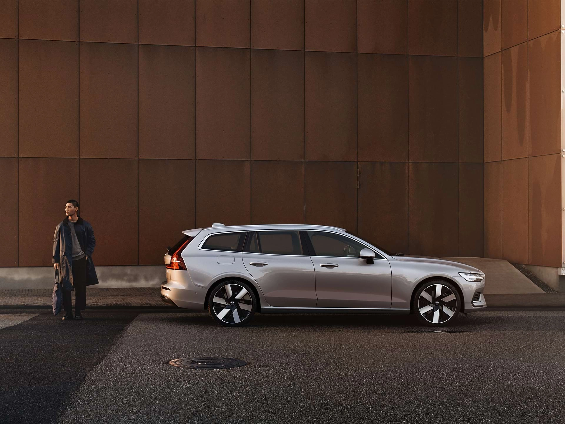 Eredas ehavalguses helklevast Volvo universaalist eemal seisev väikese kotiga mees.
