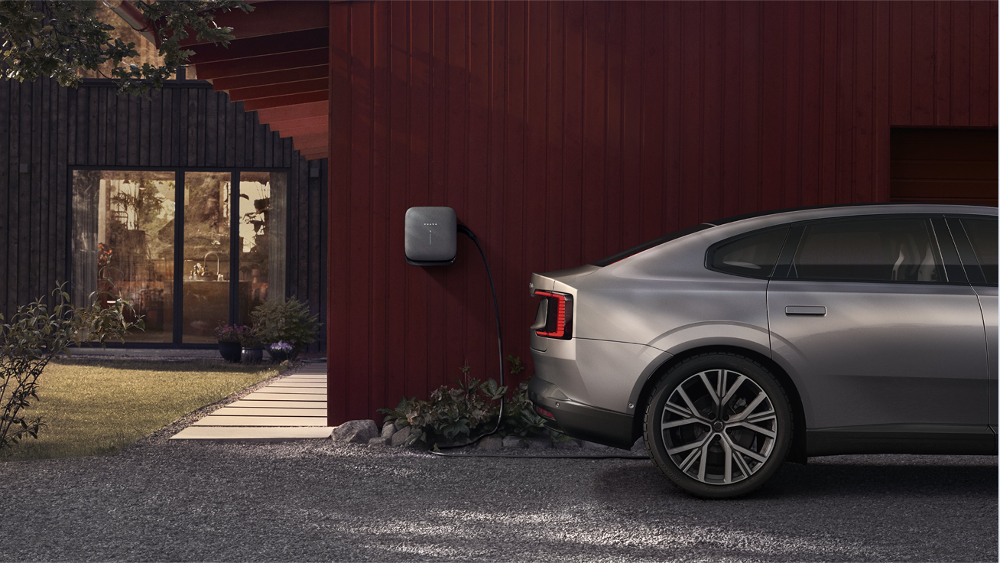 Vue latérale d’un Volvo cars électrique branché sur une borne de recharge murale contre un extérieur rouge.