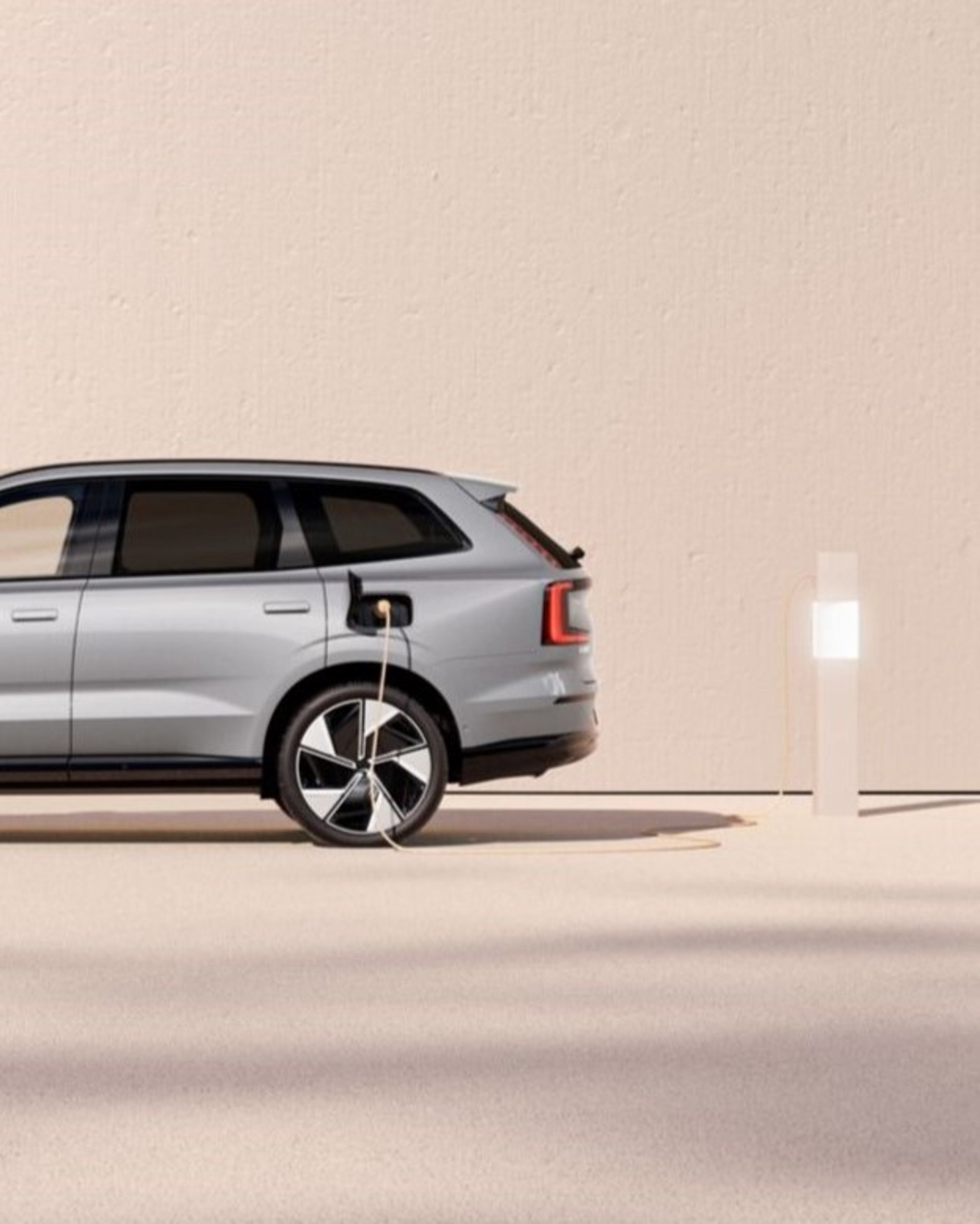 Side view of a Volvo EX90 plugged into a charging station.