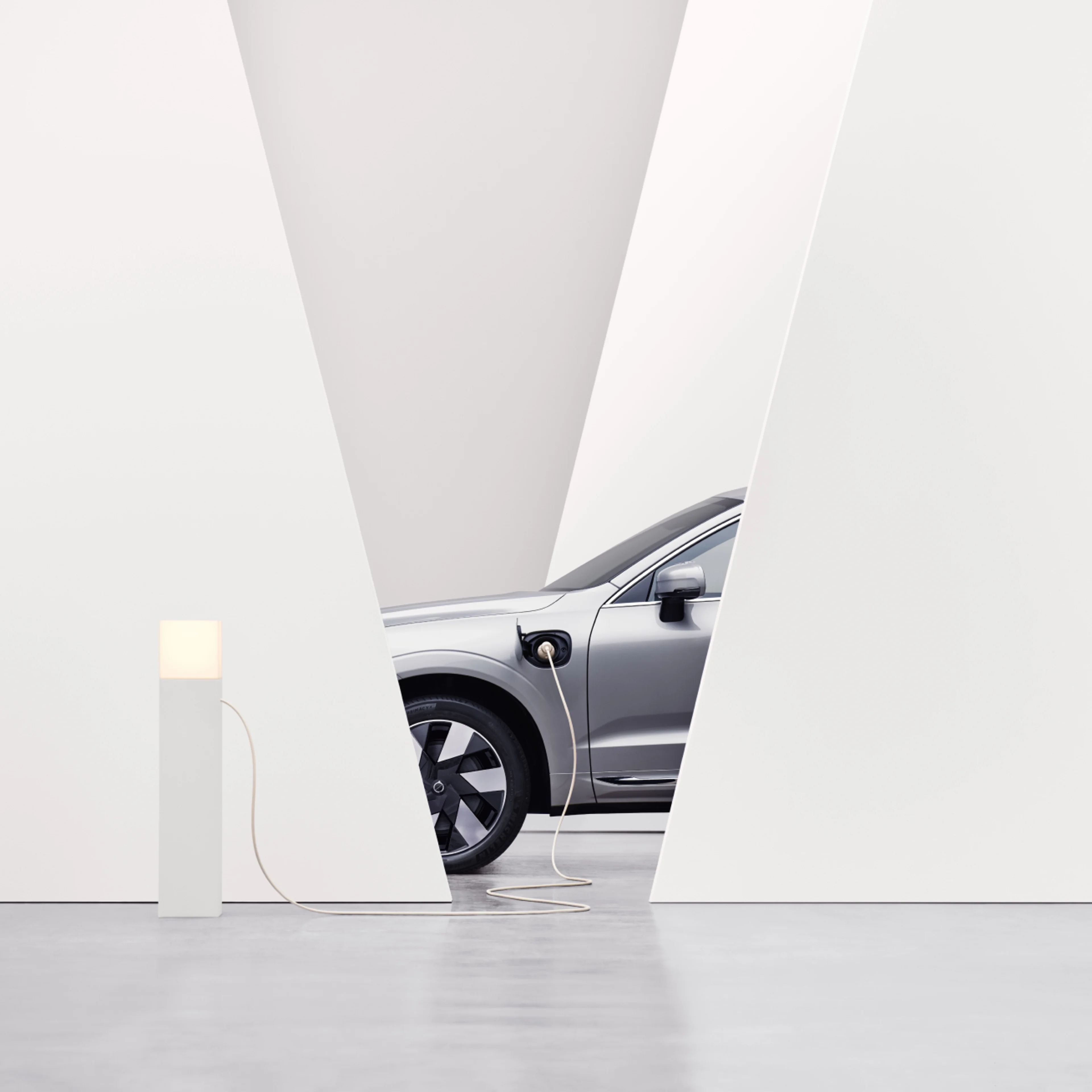 Image with a partial view of a Volvo connected to a charging point.