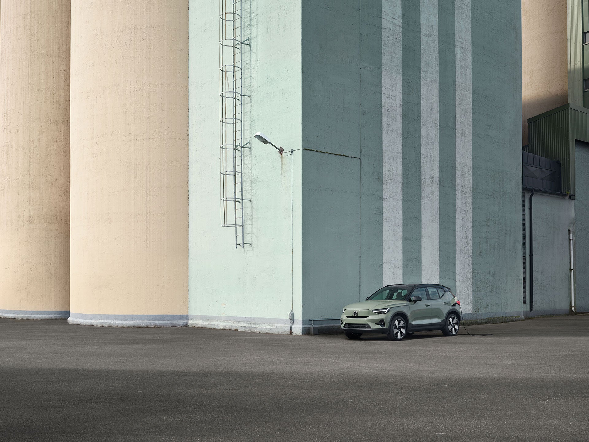 A sage green Volvo XC40 parked next to a large concrete building.