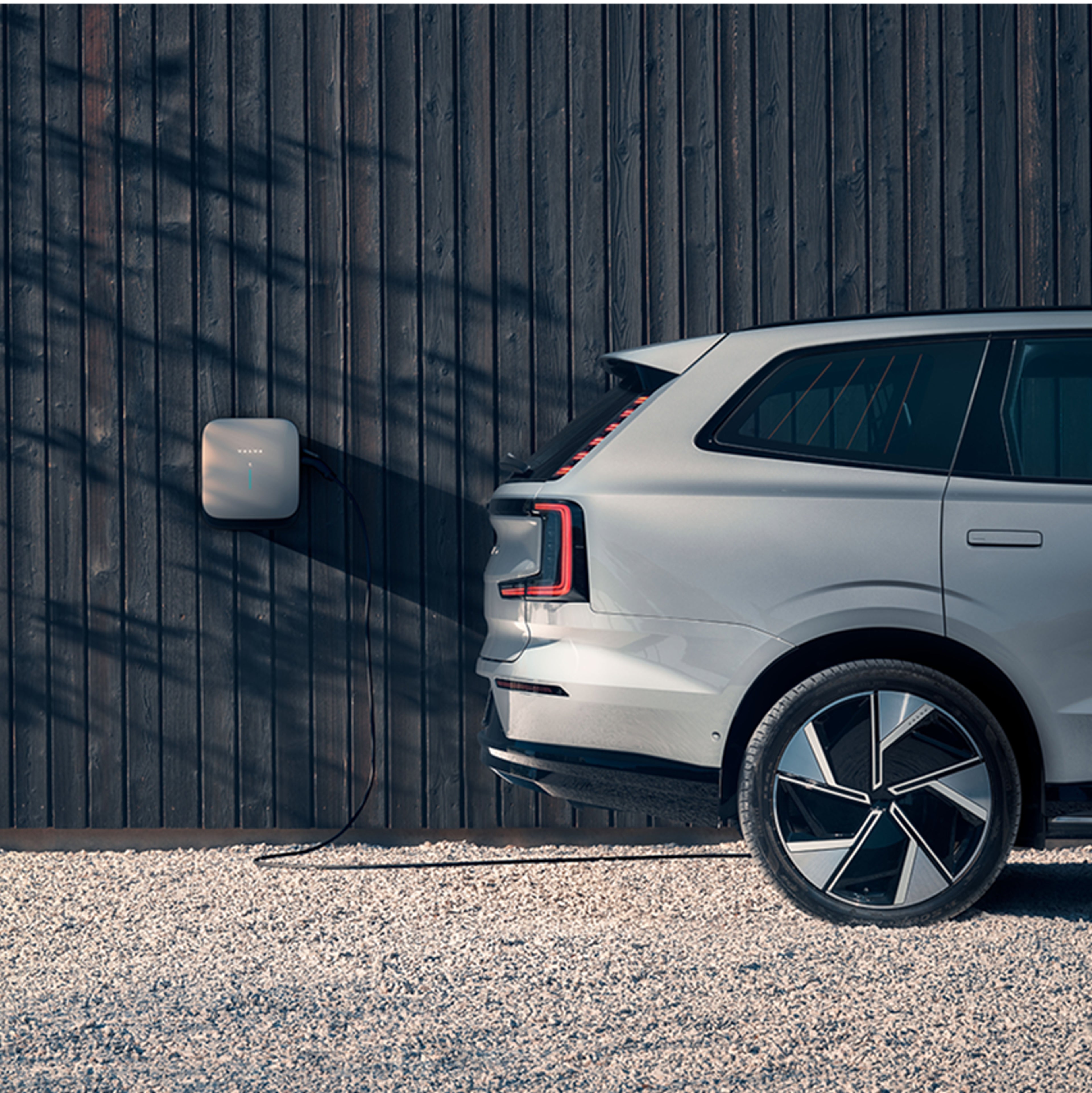Bílé SUV Volvo vedle dřevěné stěny s nástěnnou nabíjecí stanicí.