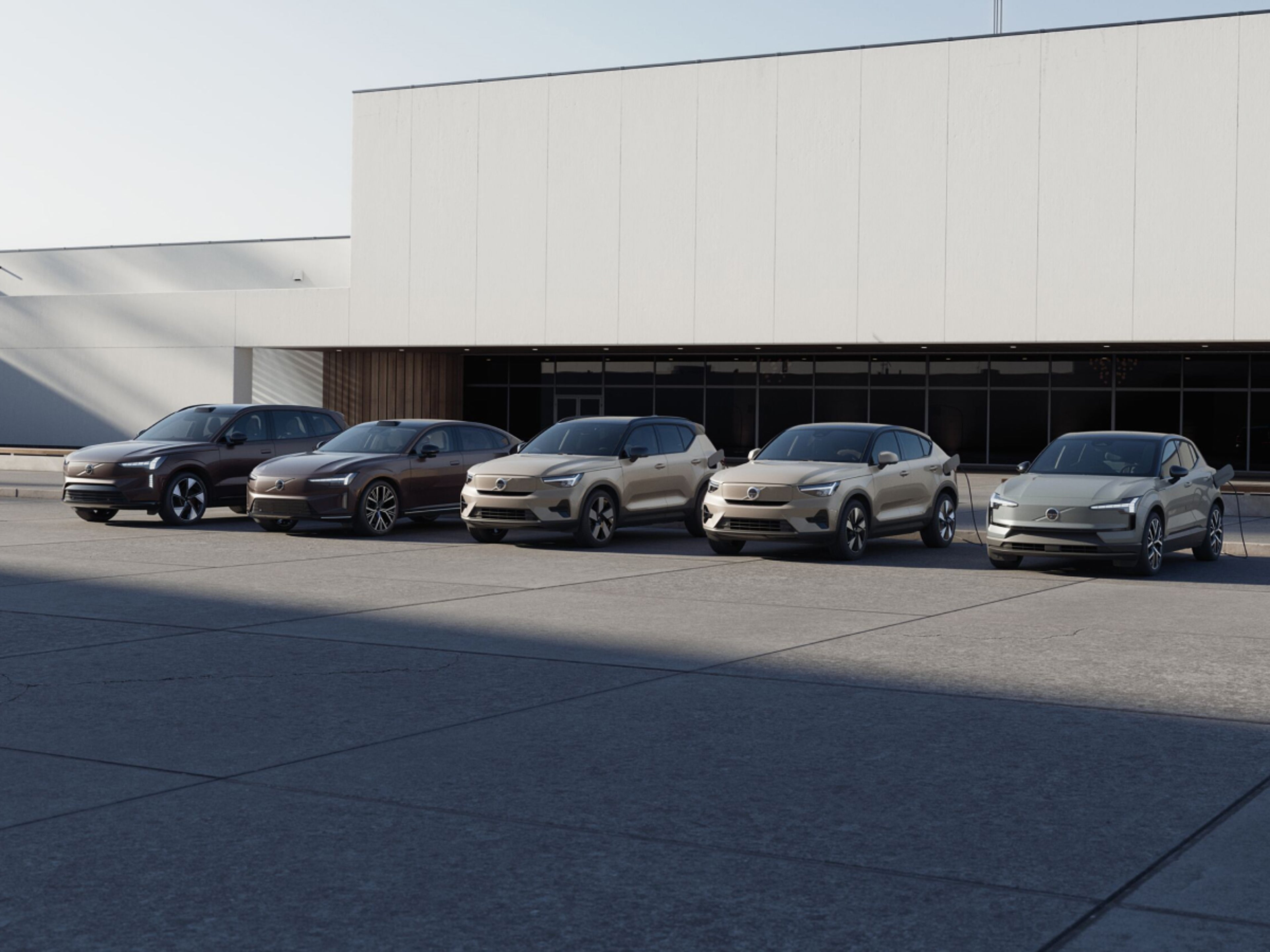 La Volvo EX90, la Volvo ES90, la Volvo EX40, la Volvo EC40 et la Volvo EX30 garées côte à côte sur un parking devant une entreprise.