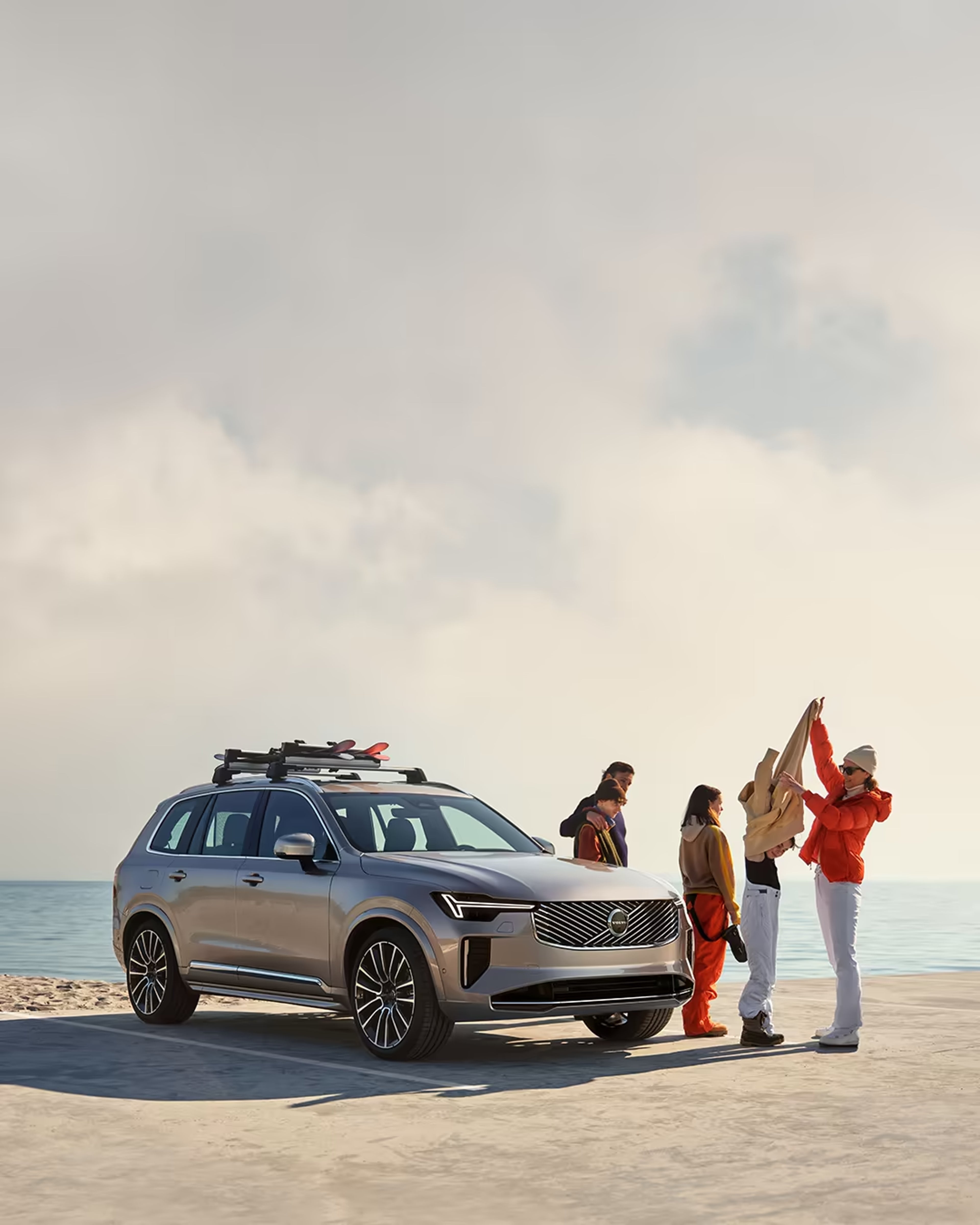 Семейство на плажа близо до Volvo XC90 Plug-in хибрид, което се преоблича от ски екипировка в бански костюми.