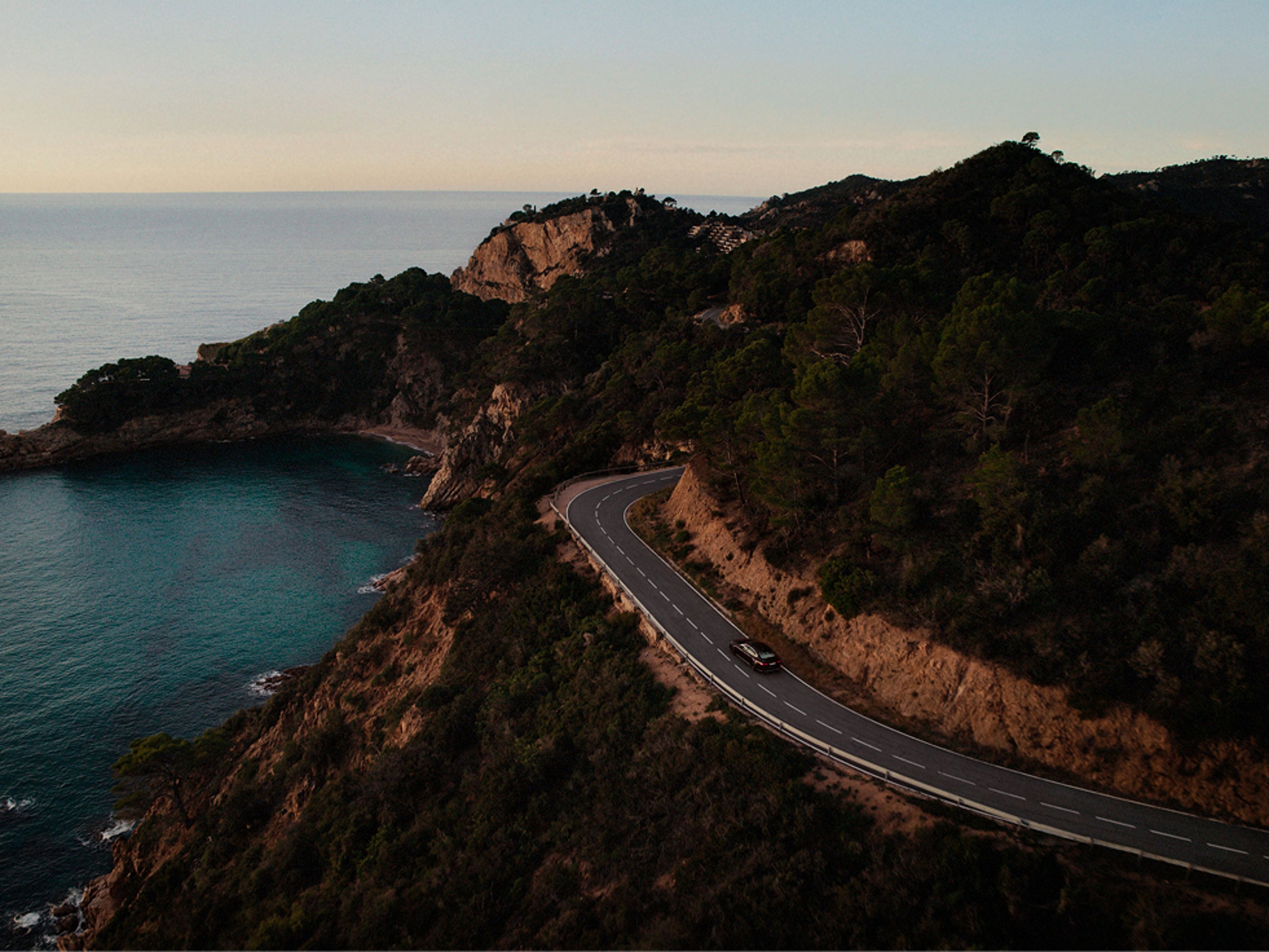 A Volvo electric car driving with the hypermiling technique along a
winding coastal road surrounded by cliffs and forest.