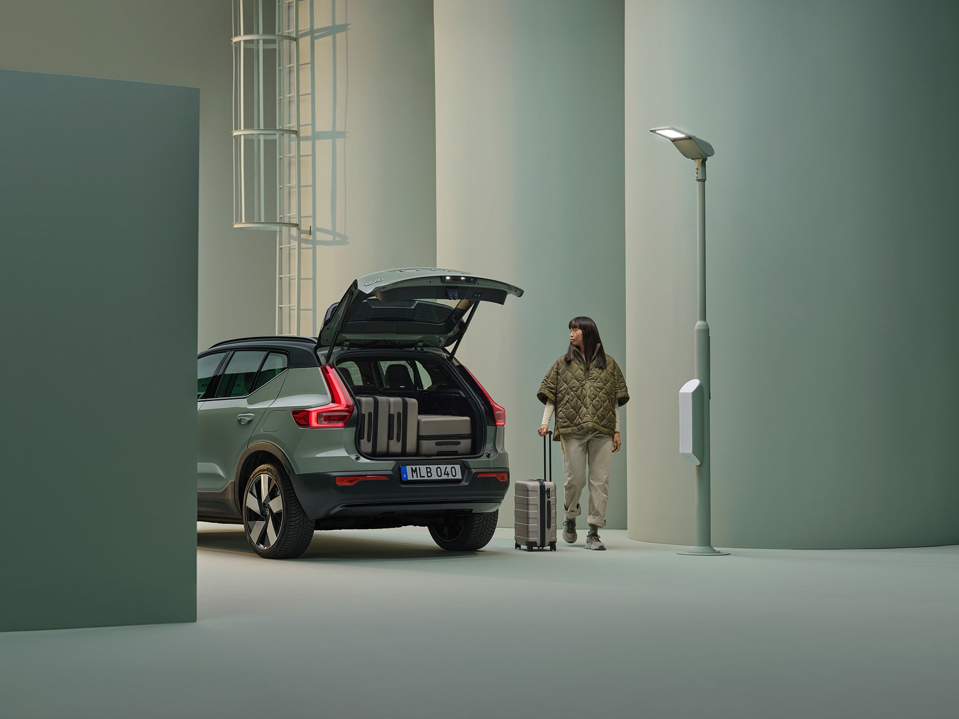 A sage green Volvo XC40 with an open tailgate and suitcases inside.