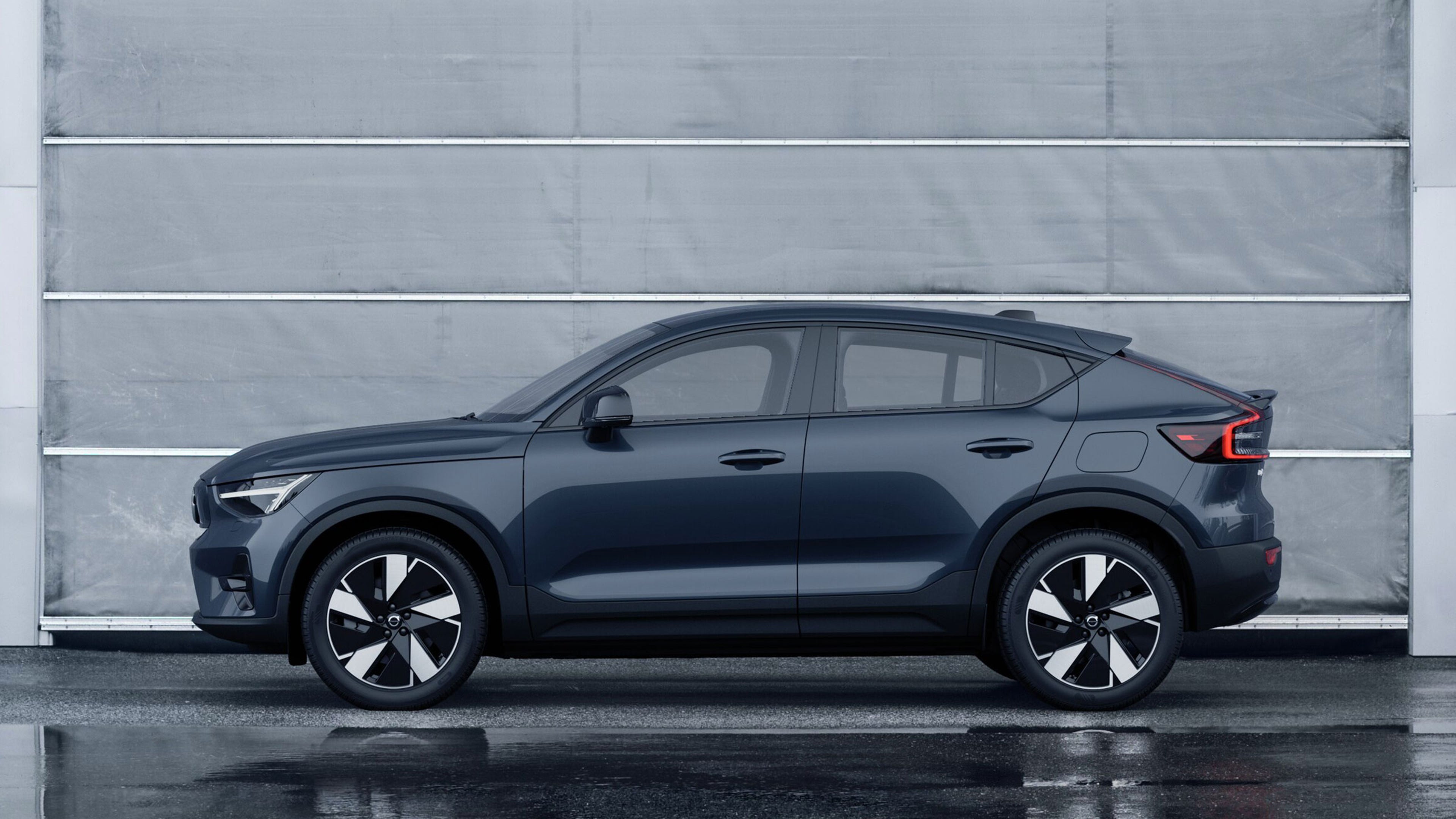 Denim blue -värinen Volvo EC40 täyssähköauto. Taustalla vihertävä betoniseinä.