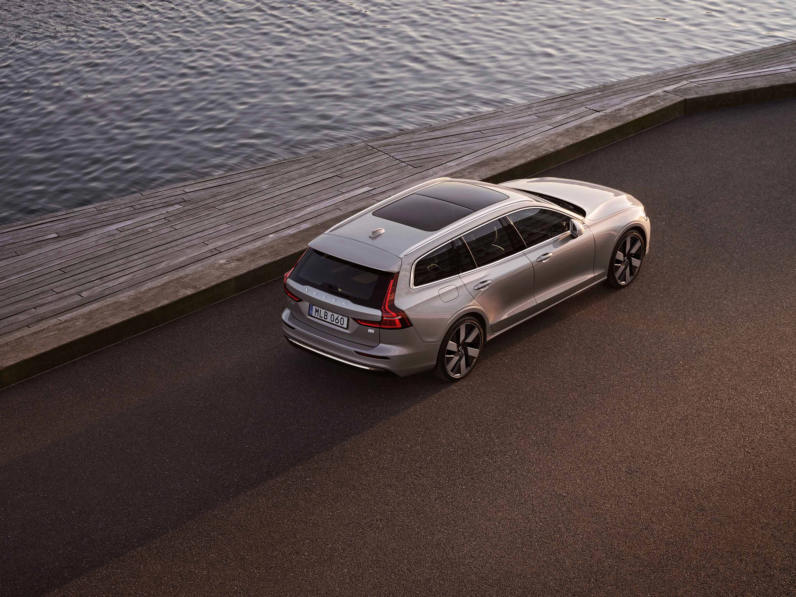 Wide shot of a Volvo V90 wagon in Bright Dusk driving along a mountainous road overlooking a glittering fjord.