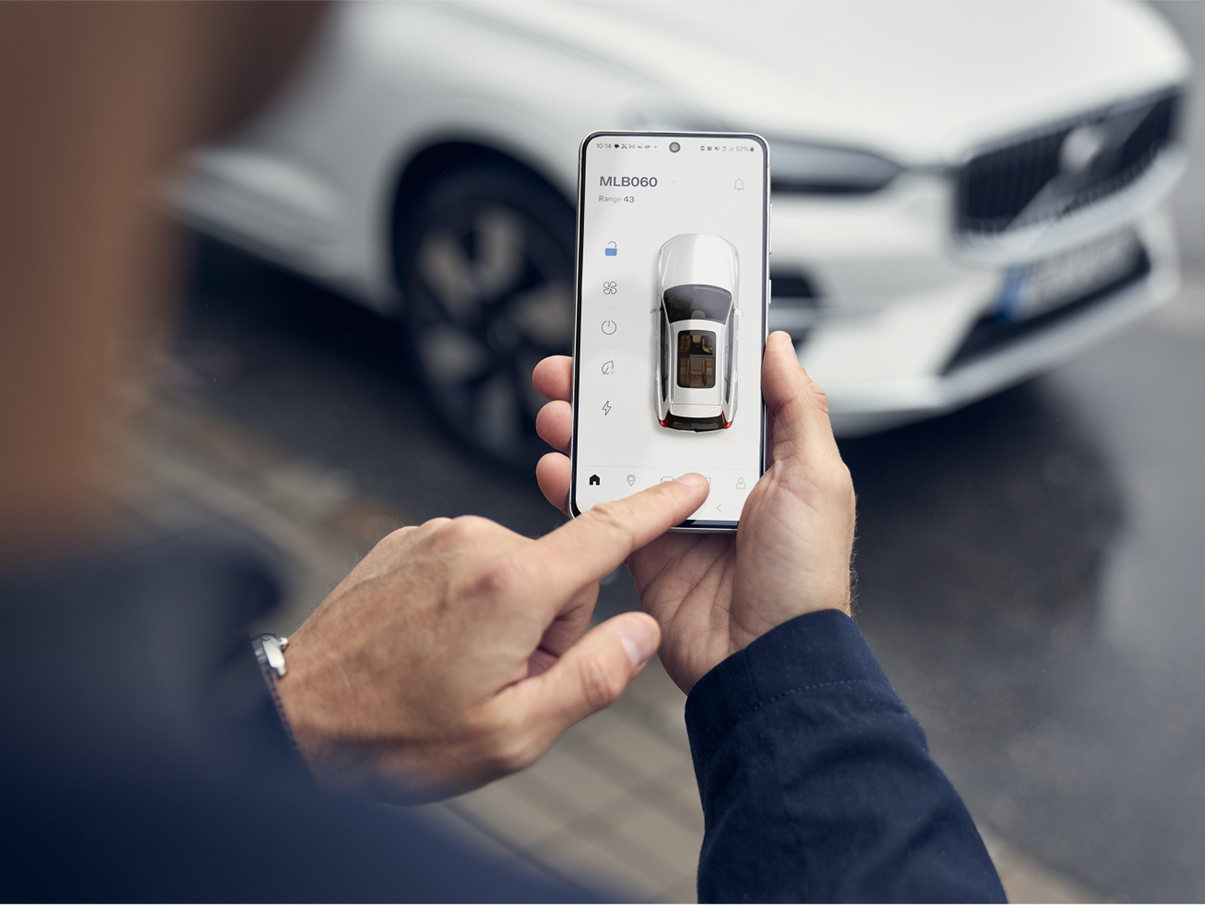 Person using the Volvo Cars app on a smartphone to access remote features of their vehicle, with a white Volvo visible in the background.