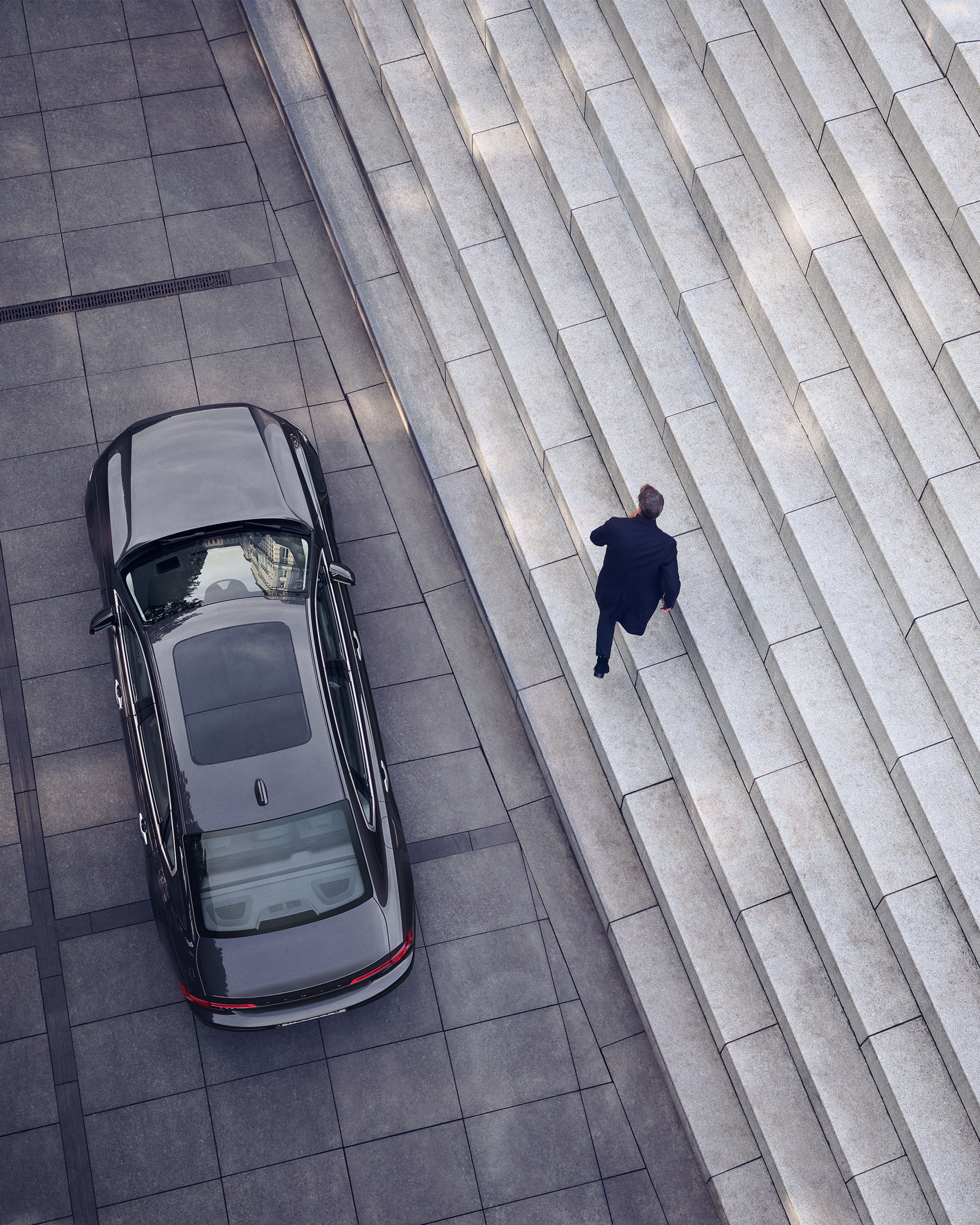 Bird's view of a man leaving his Volvo S90 parked beside graphical marble stairs.