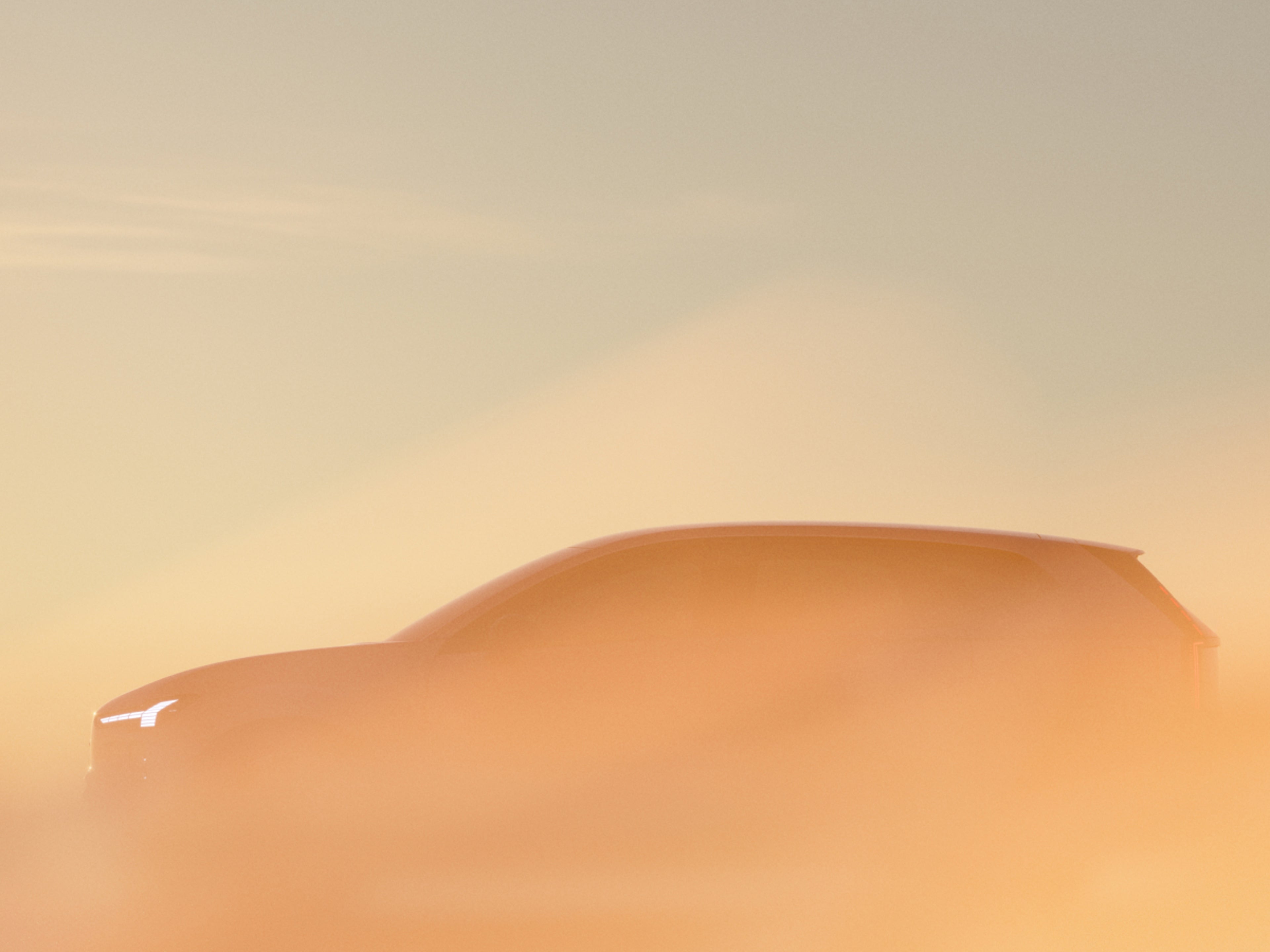 Silhouette d'une Volvo EX60 enveloppée dans un épais brouillard orange au lever du soleil, avec les phares Thor's Hammer illuminés.