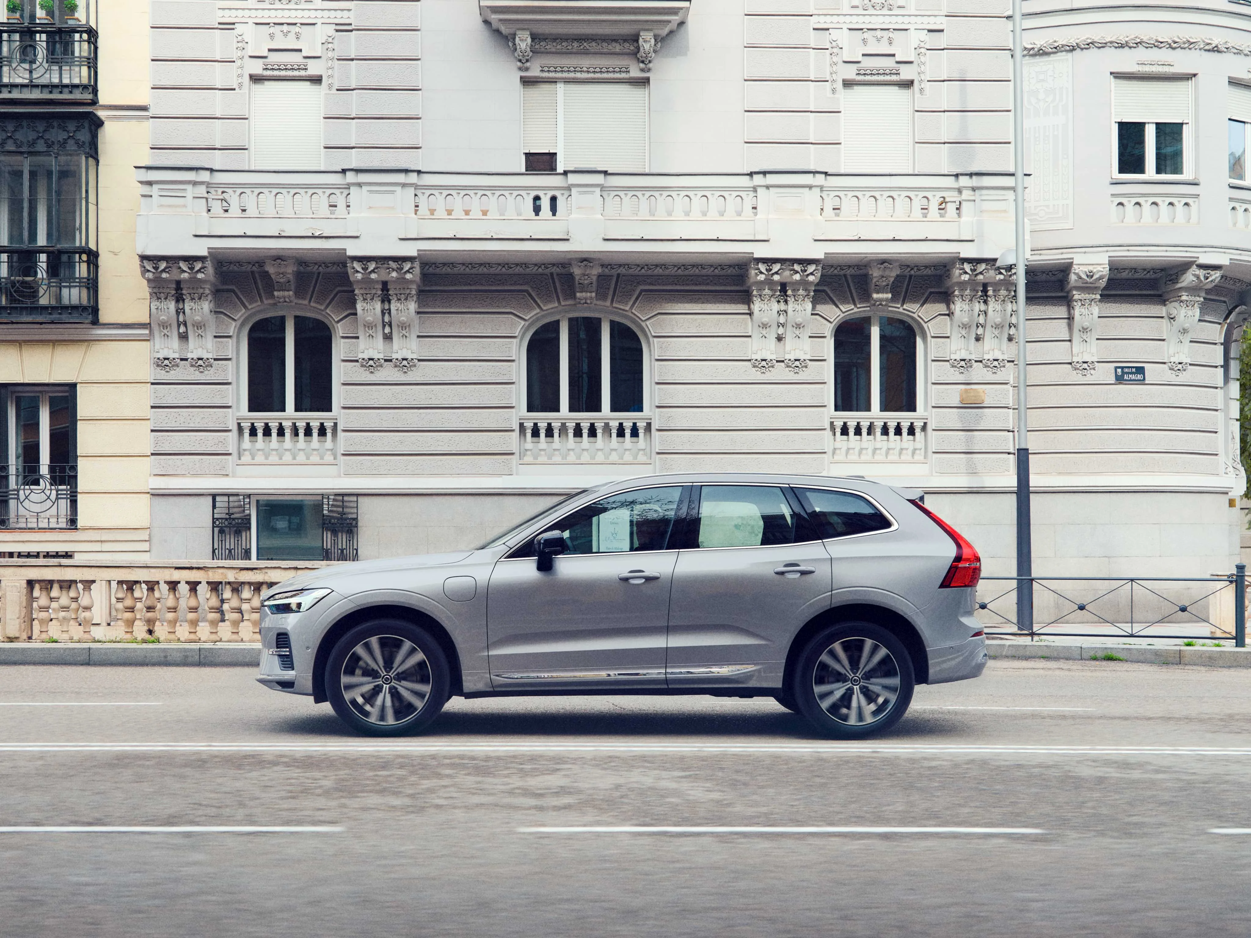 Wide angle view of a Volvo XC60 in Silver Dawn drives down a European city street.