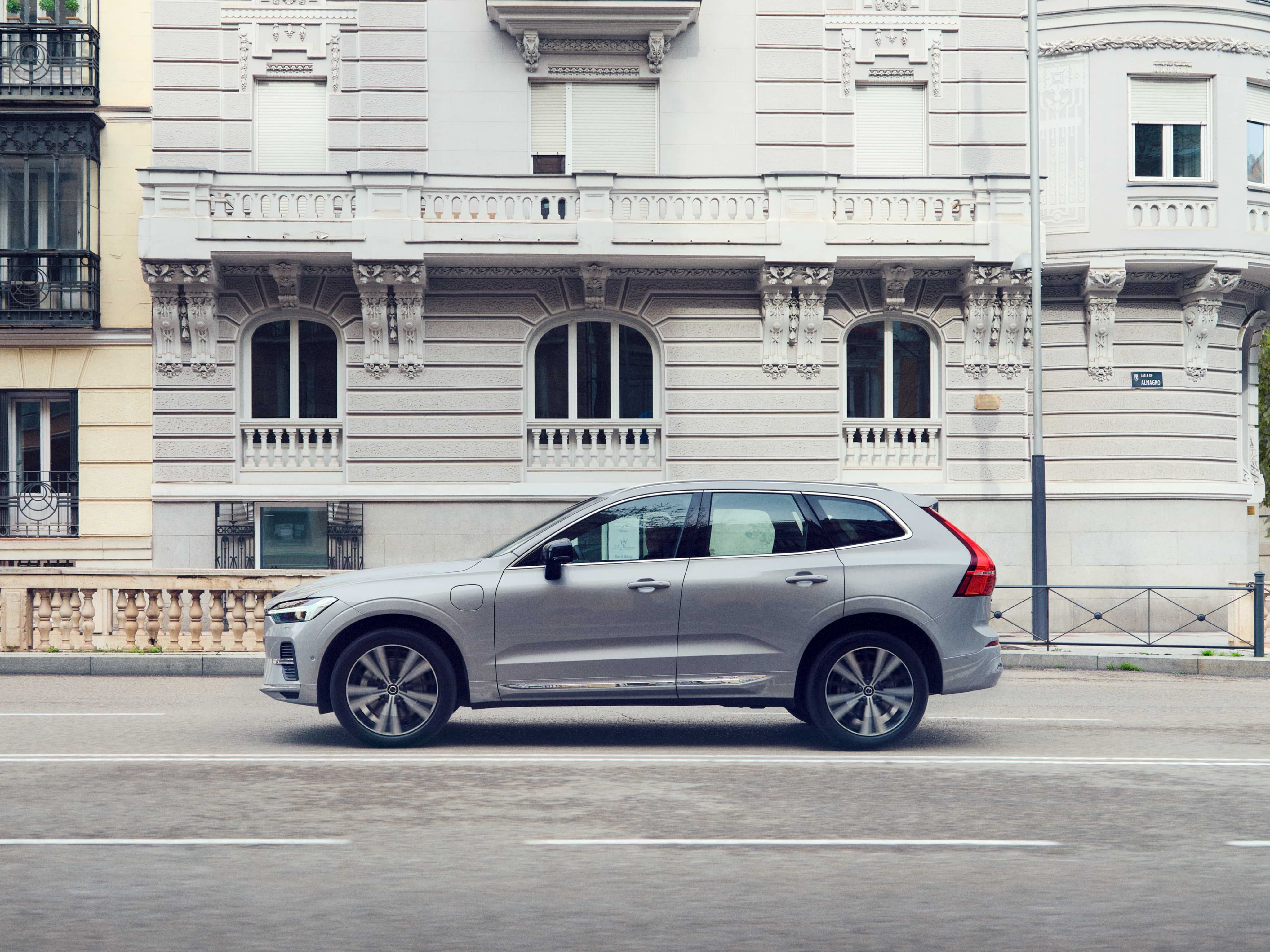 Wide angle view of a Volvo XC60 in Silver Dawn drives down a European city street.