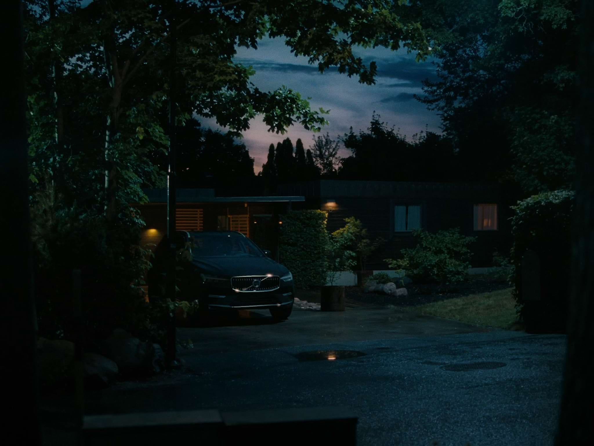 A dark Volvo SUV sits parked on a suburban driveway at dusk.