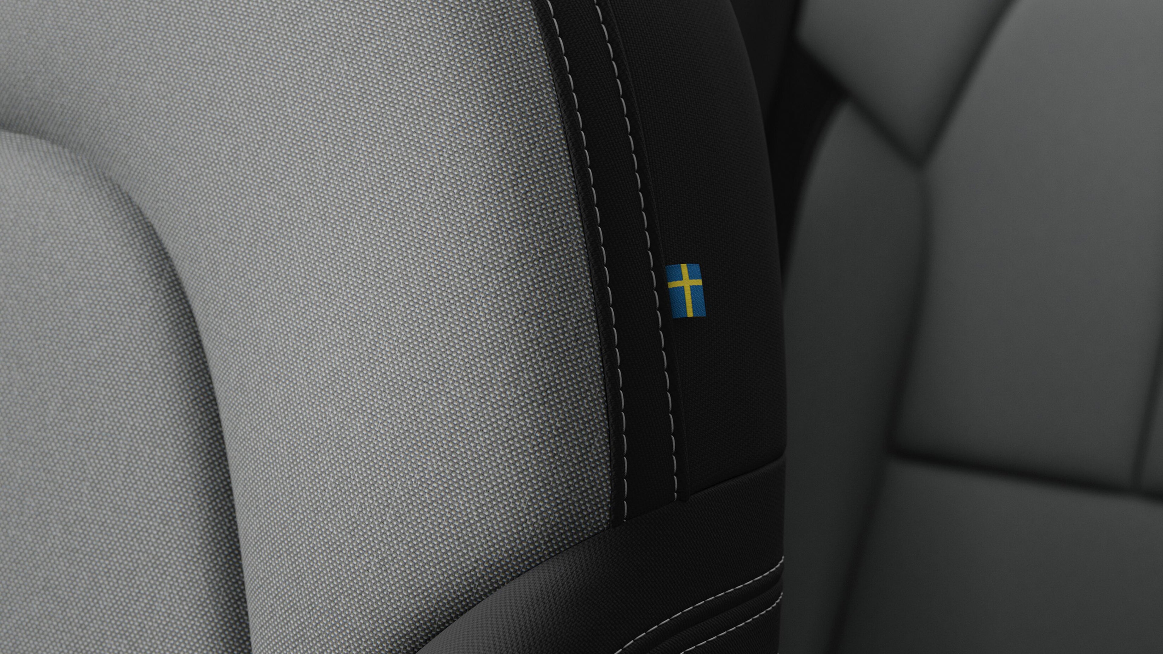 Ein grau melierter Sitz im Innenraum eines Fahrzeugs mit Fokus auf die Schwedenflagge, ein kleines Emblem an der Naht des Sitzes.