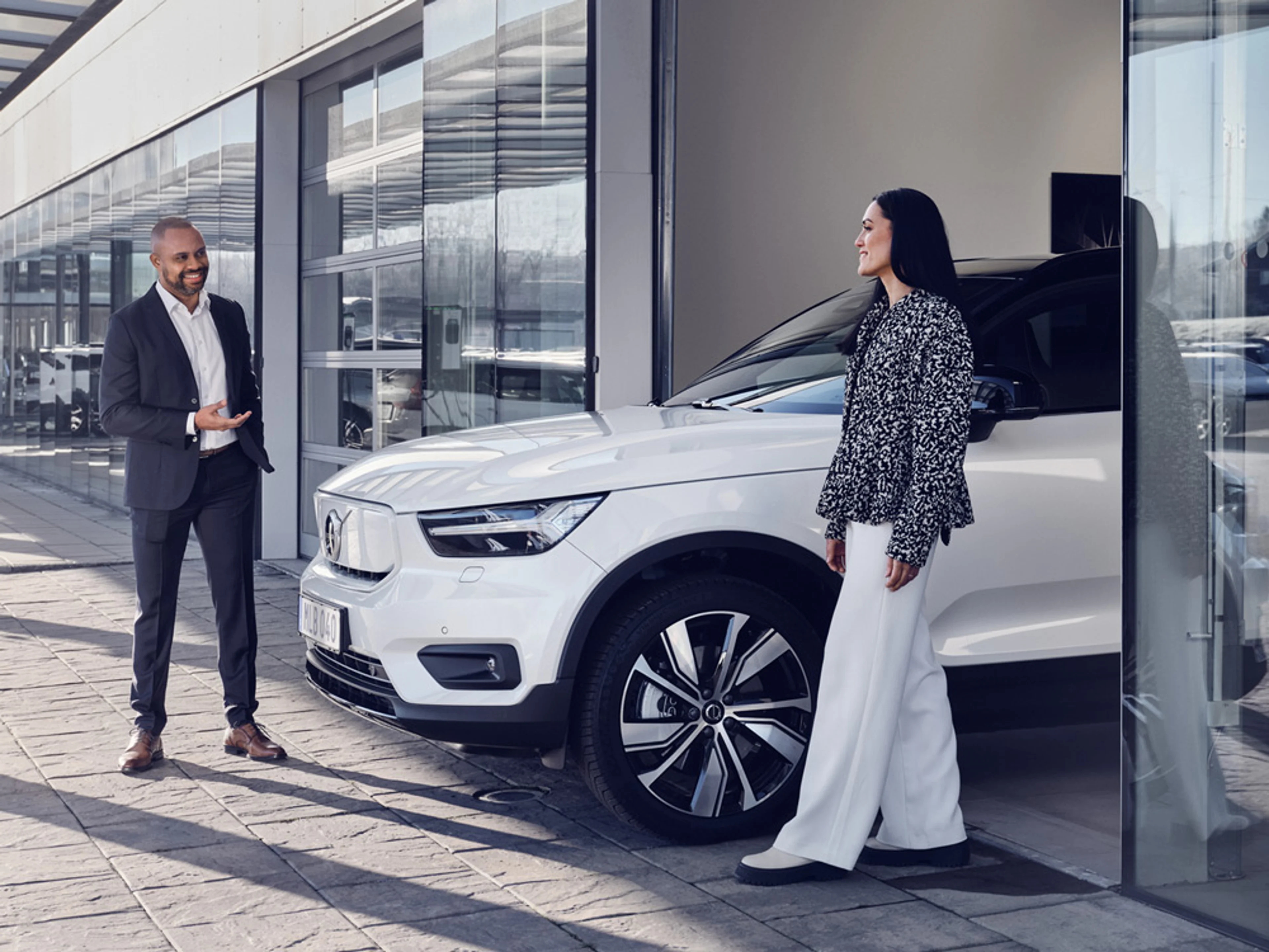 Un homme et une femme en costume se tiennent à côté d'une Volvo électrique chez un concessionnaire Volvo.