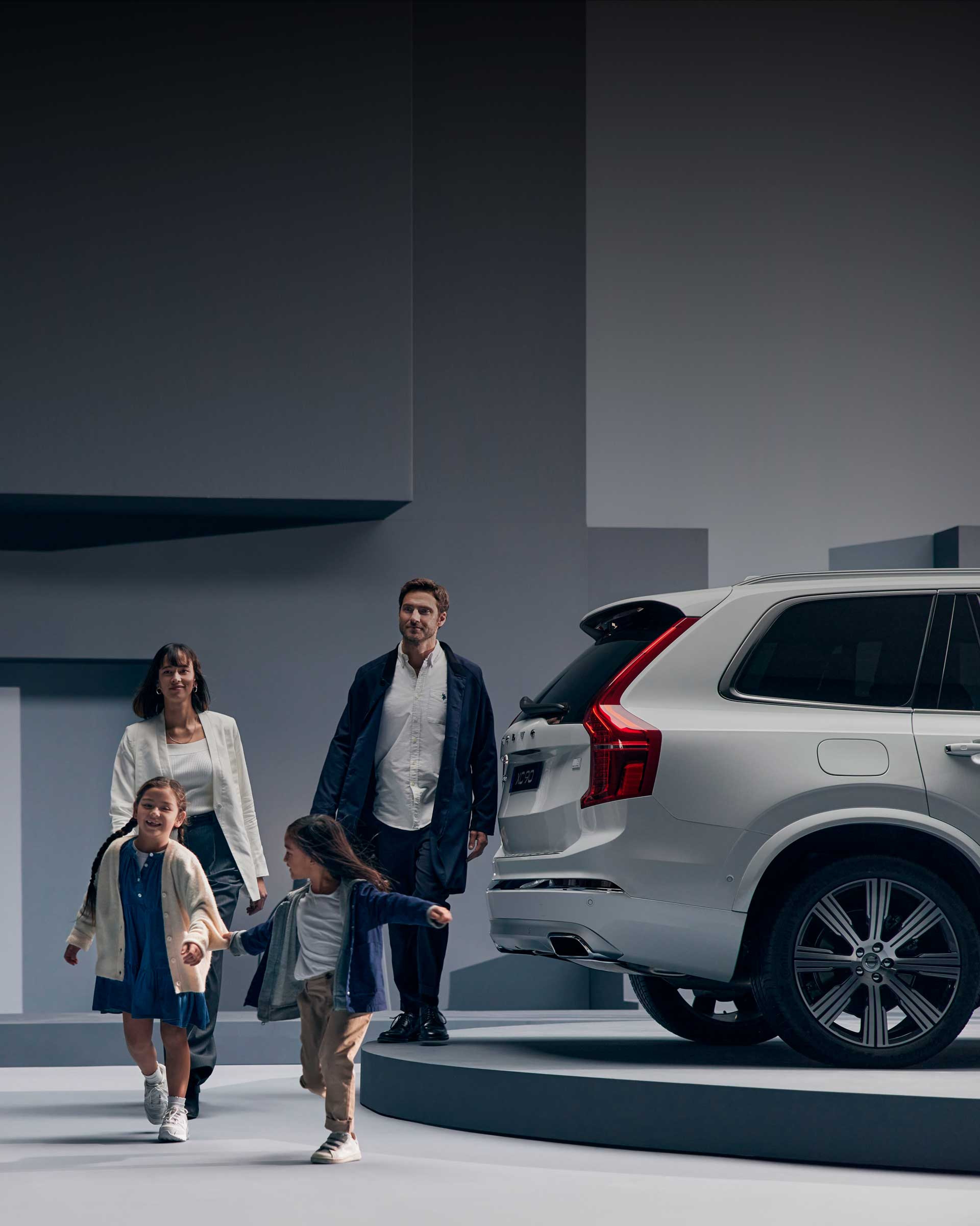Una familia caminando al lado de un Volvo XC90 sobre un fondo gris.