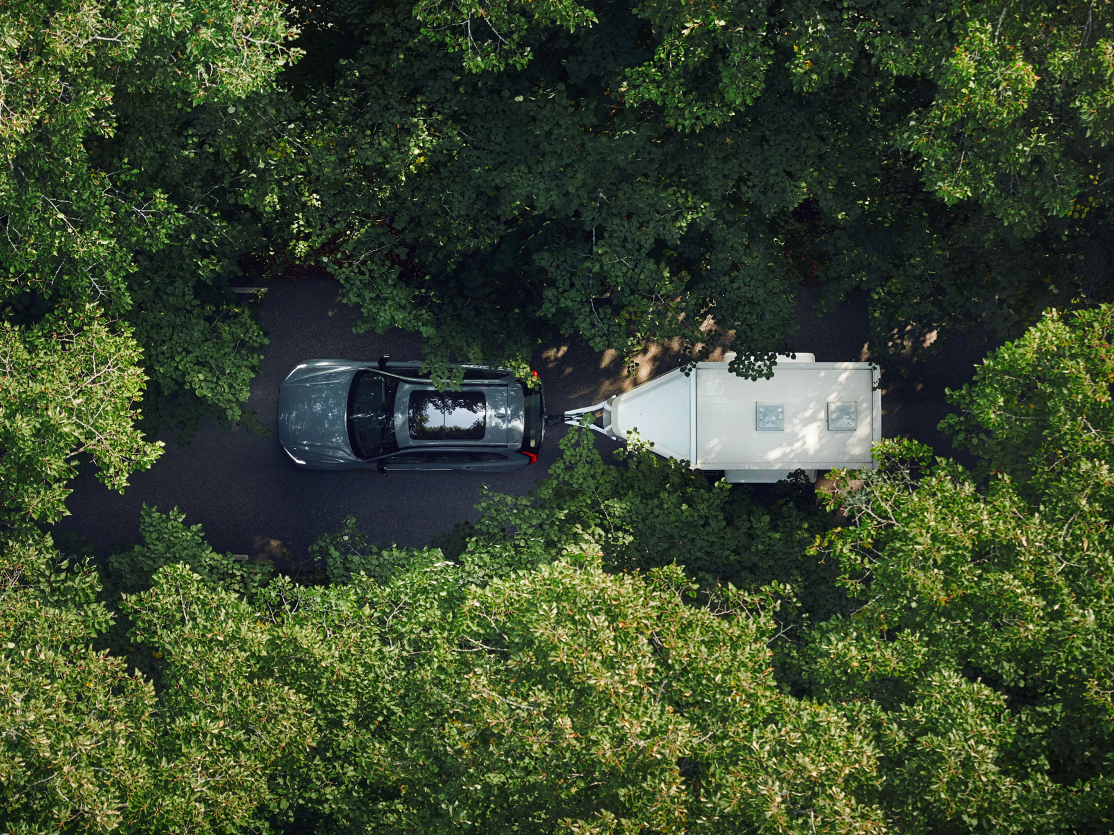 Vue aérienne d'une voiture tractant une remorque sur une route étroite entourée d'arbres verts