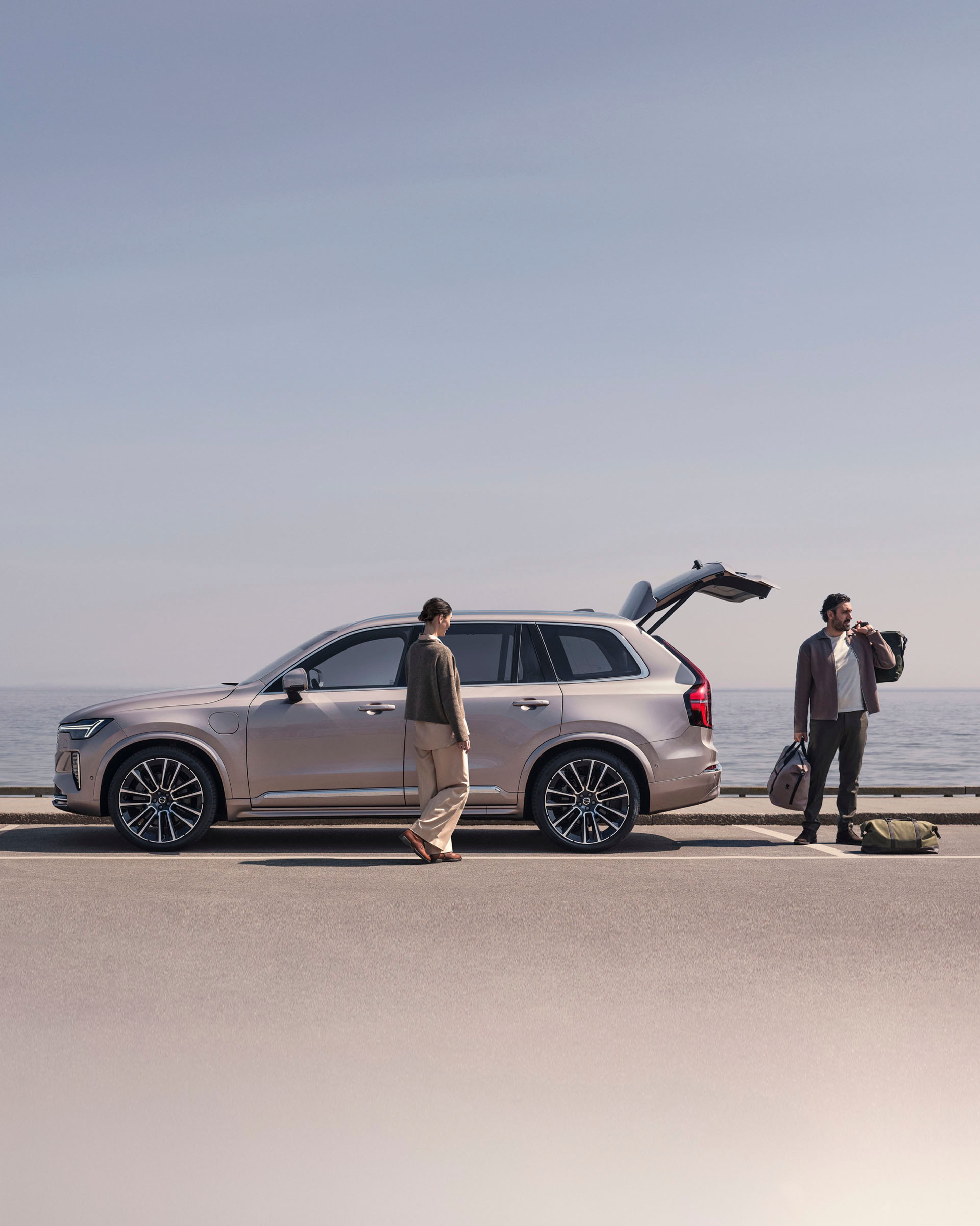 Una pareja junto a un Volvo XC90 híbrido enchufable junto al mar