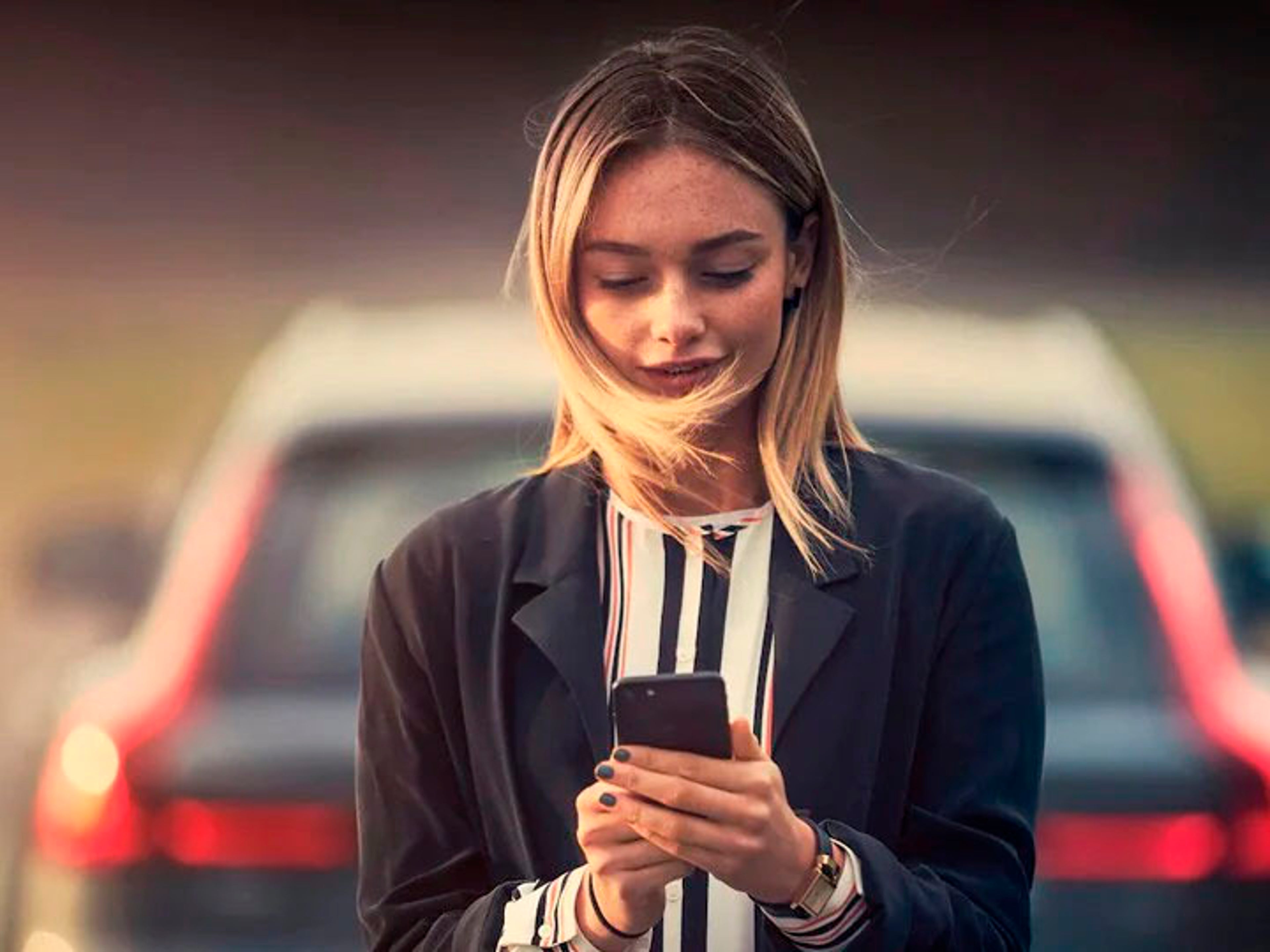 Una mujer consultando su móvil y un Volvo al fondo