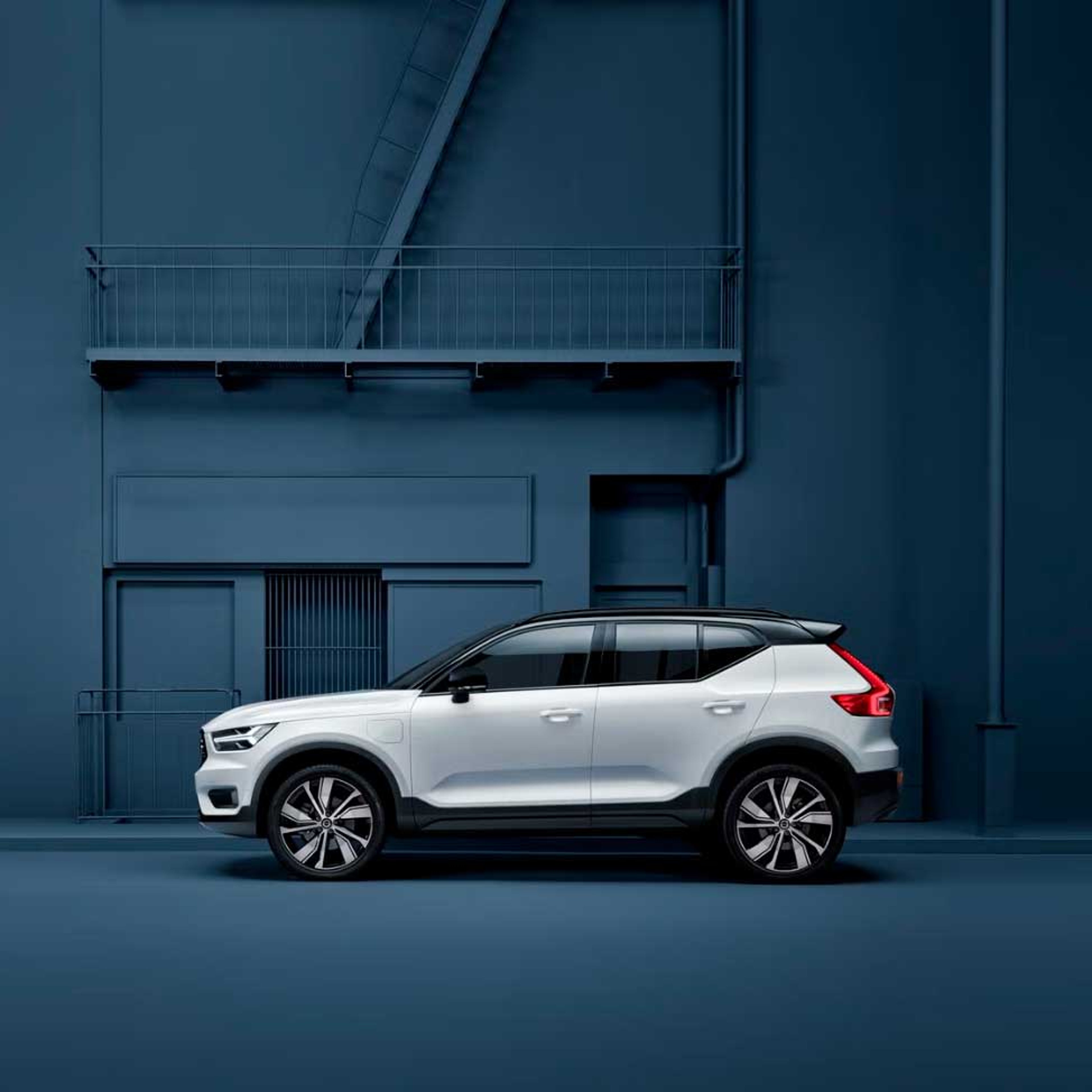 Elegant hvid Volvo SUV parkeret foran en minimalistisk, mørkeblå industrivæg. En moderne, rolig stemning fremhæver bilens raffinerede design.