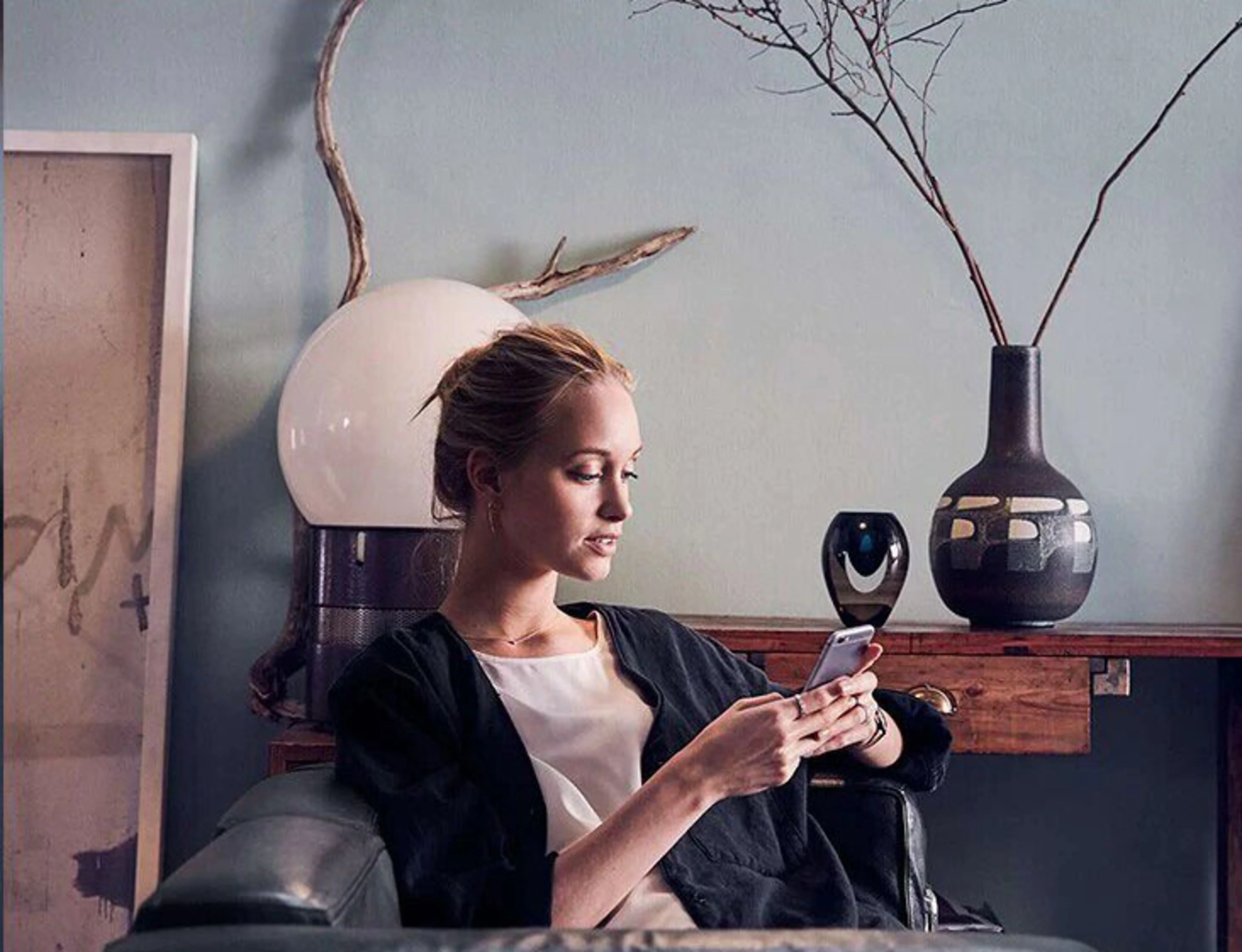 Une femme assise dans un fauteuil confortable regarde son smartphone, dans un espace élégamment décoré avec des éléments de design.
